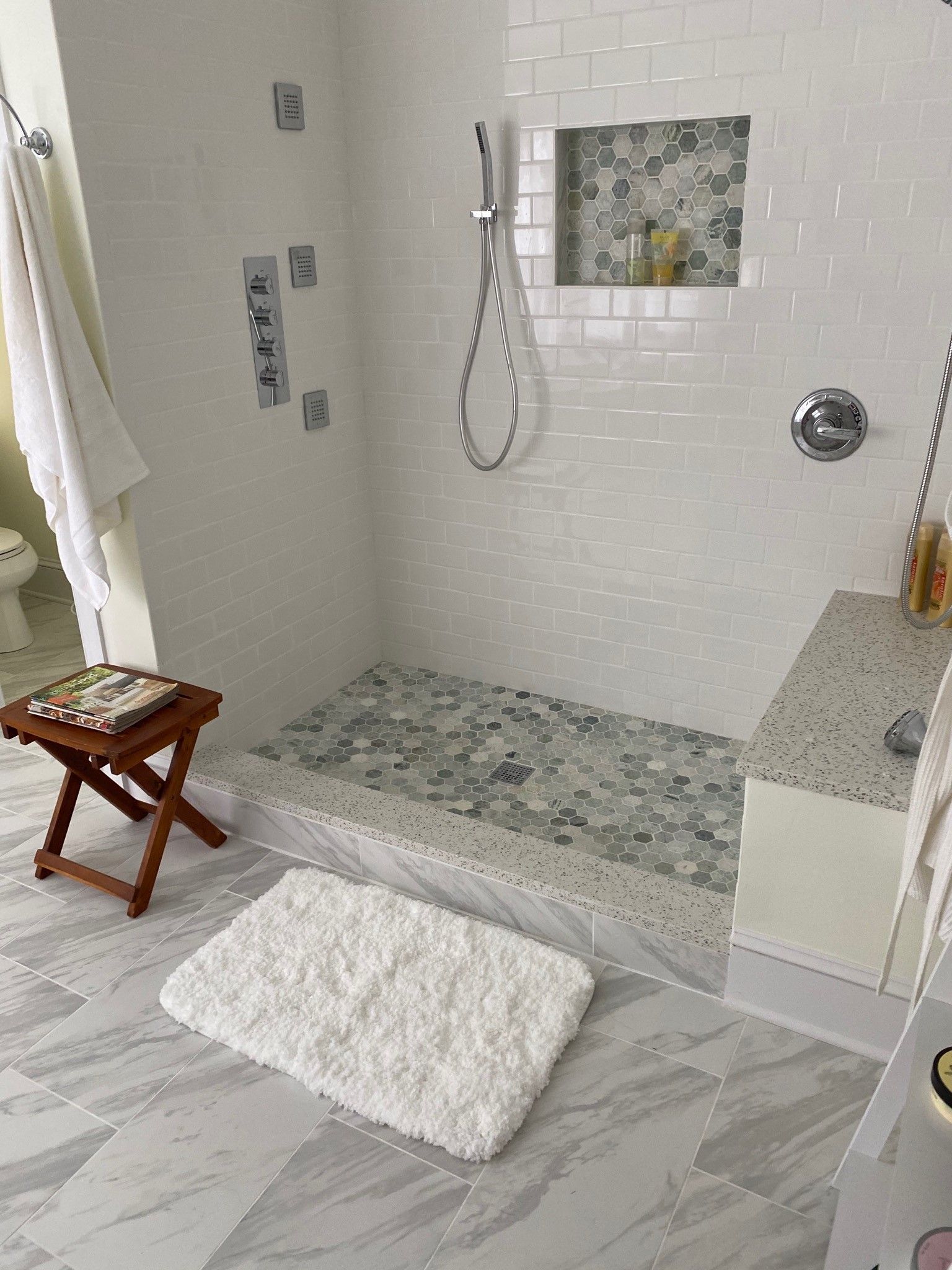 Bathroom with white tiled walls, stone shower floor, and a white bath mat.