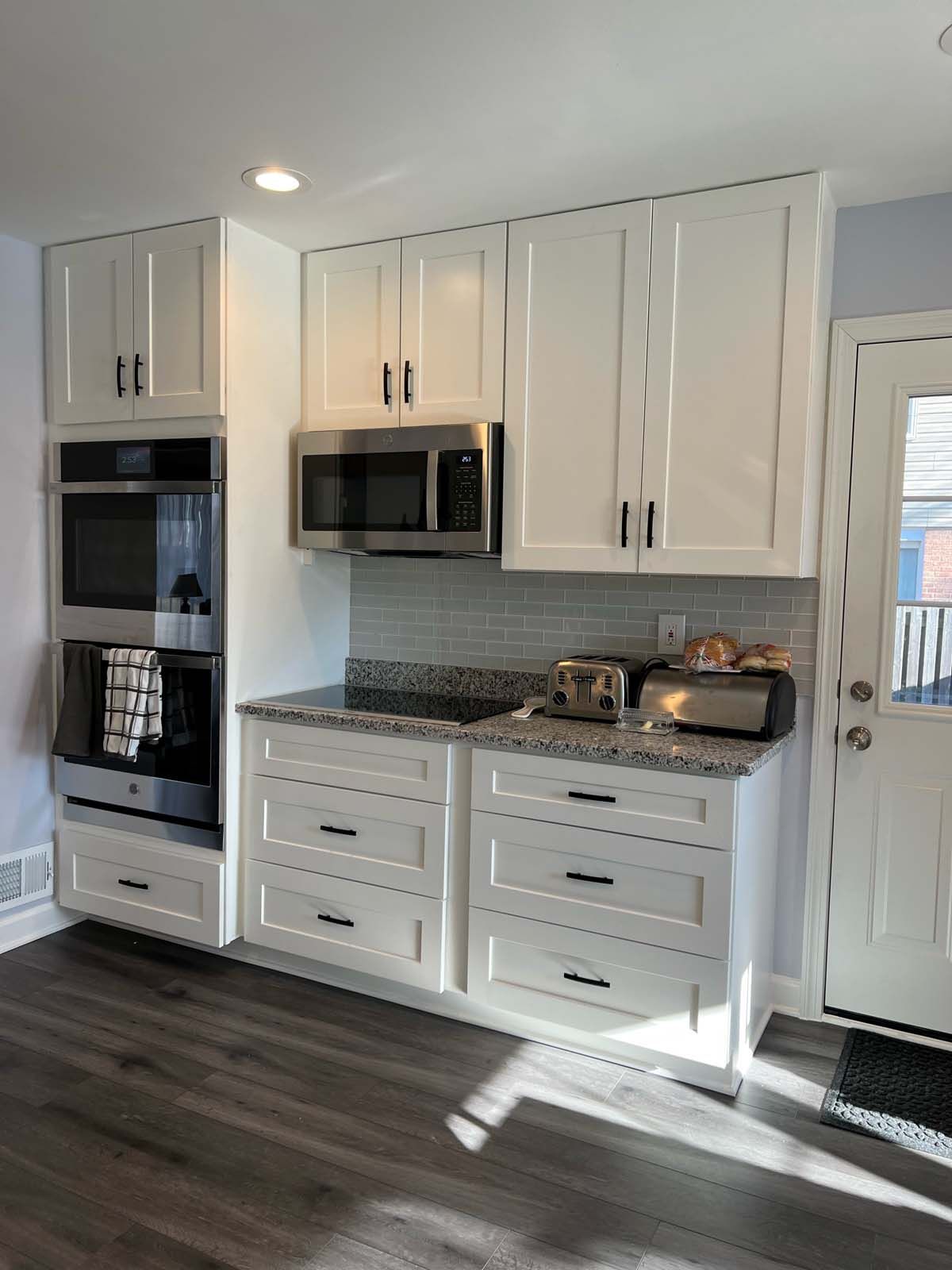 White kitchen cabinets with granite countertop, stainless steel appliances, and dark wood flooring.