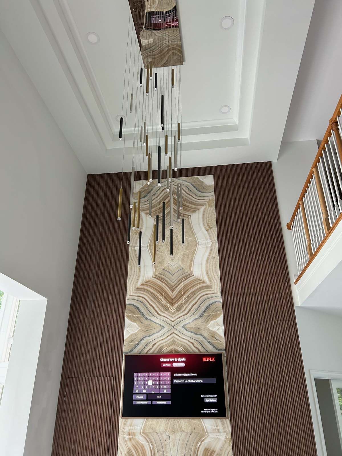 A modern living room with a decorative light fixture, a wall-mounted TV, and a staircase.