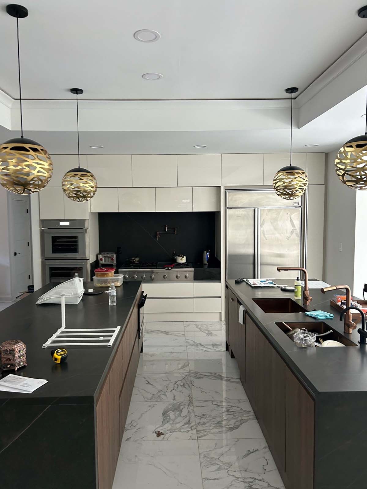 Modern kitchen with two islands, light cabinets, and gold pendant lights. Stainless steel appliances. Marble floor.