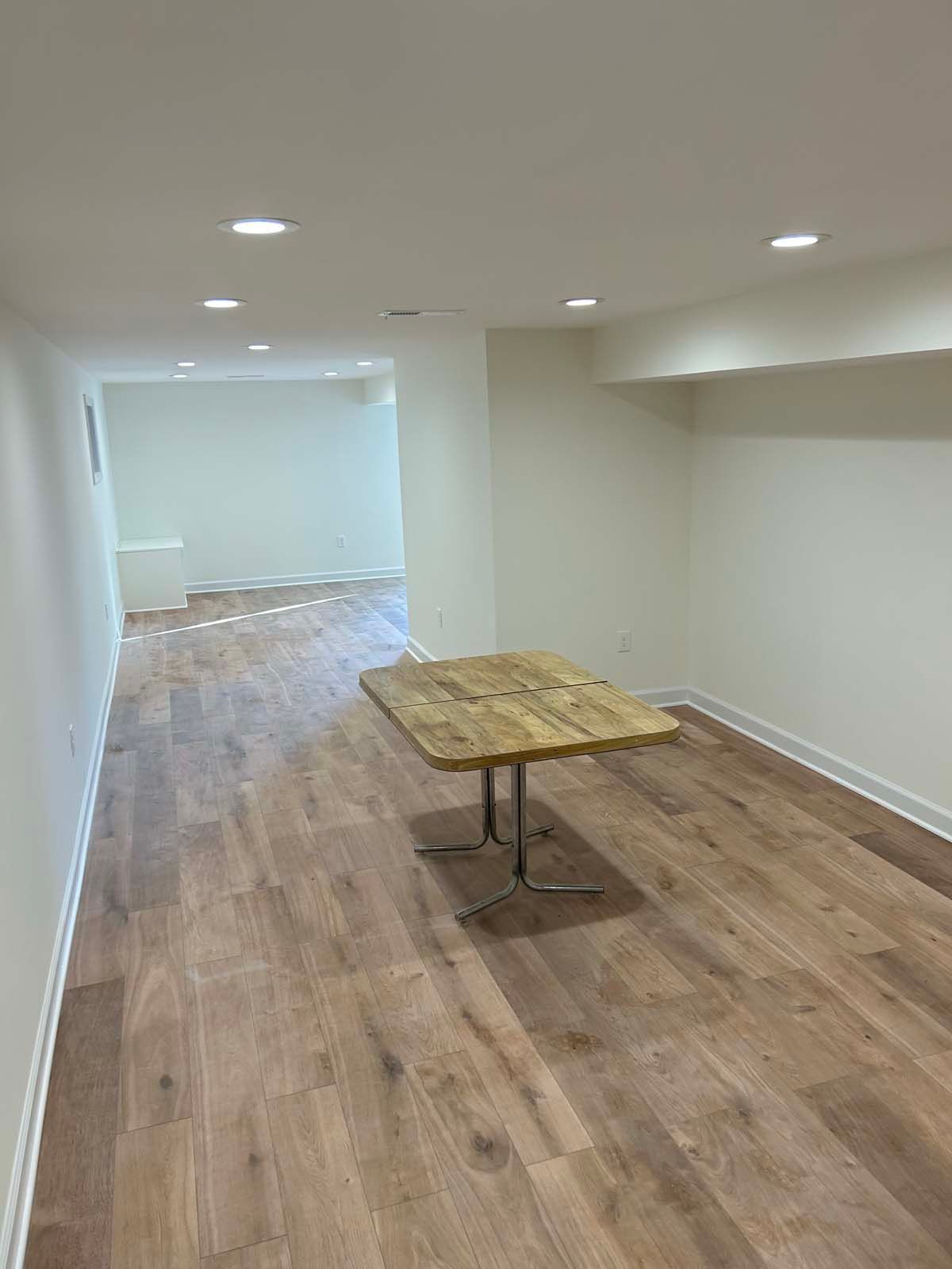 Empty room with wood flooring, white walls, and a rustic wooden table in the center.