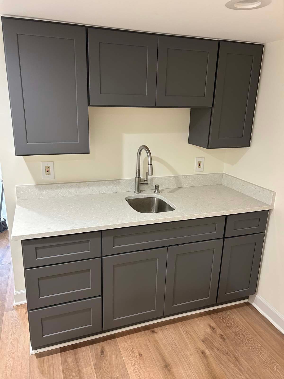 Gray cabinets with a white countertop and stainless steel sink in a small kitchen.