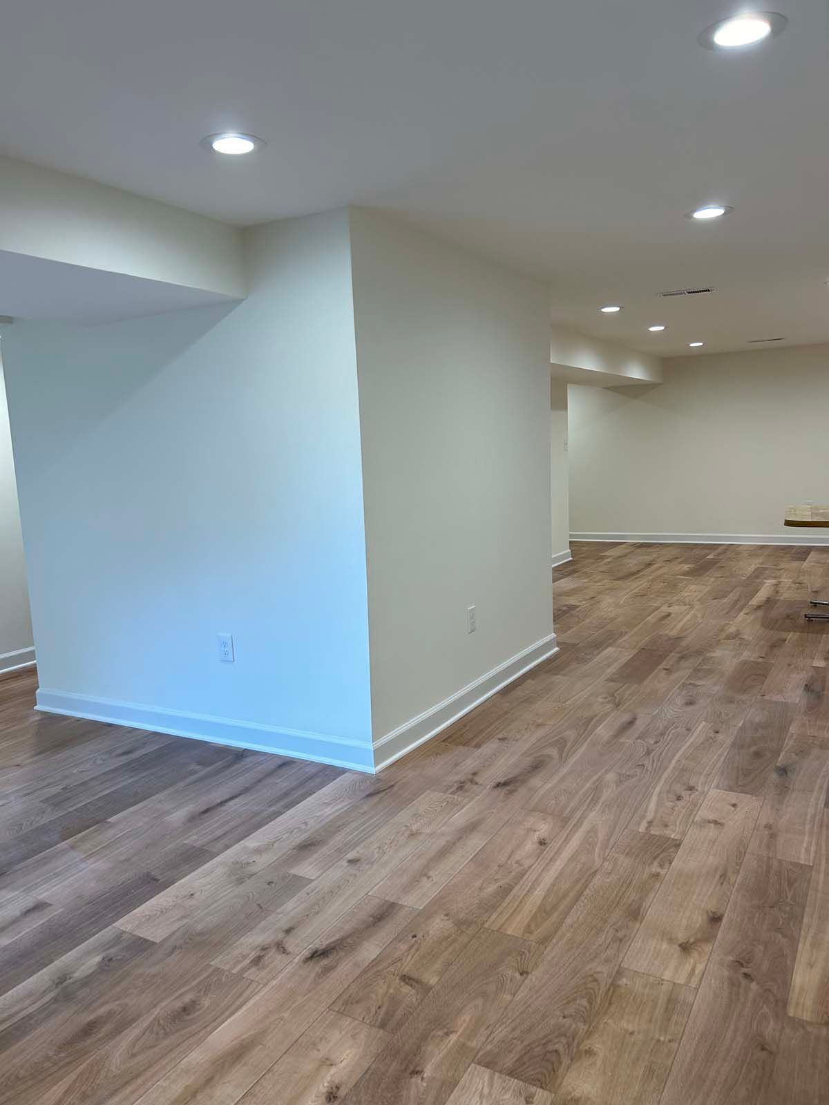Beige basement interior with wood-look flooring, recessed lighting, and white walls.