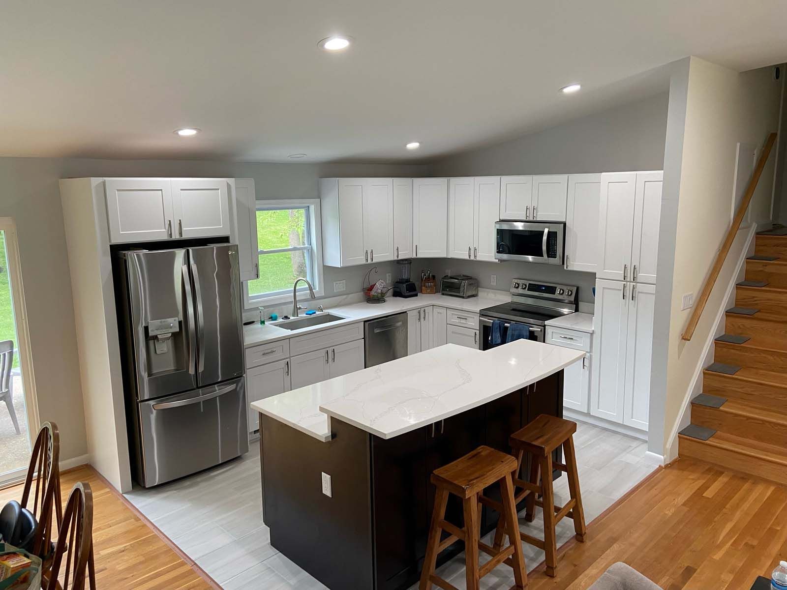 Modern kitchen with white cabinets, stainless steel appliances, and a dark island with stools.