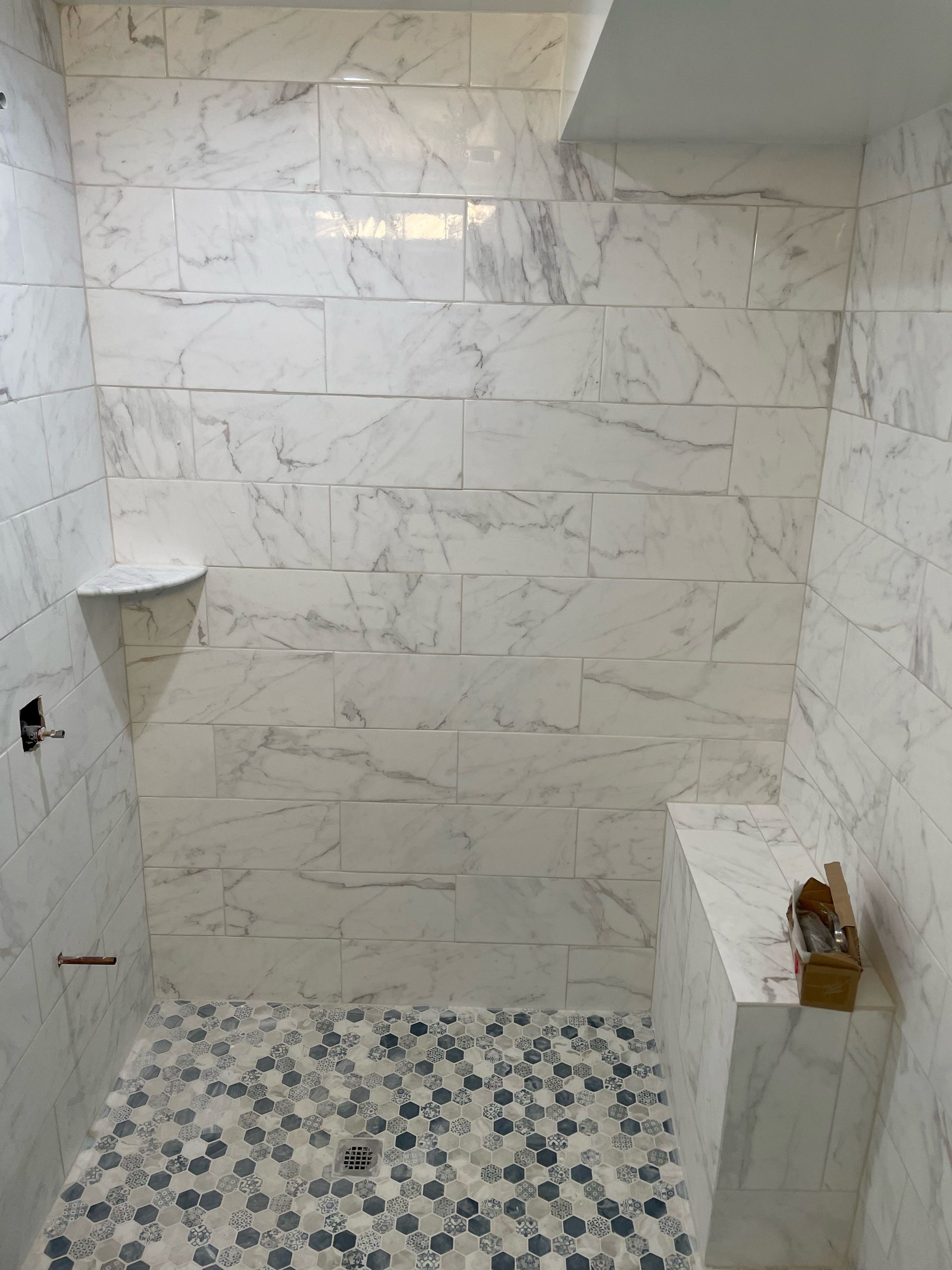 White marble-tiled shower with shelf, bench, and mosaic floor.