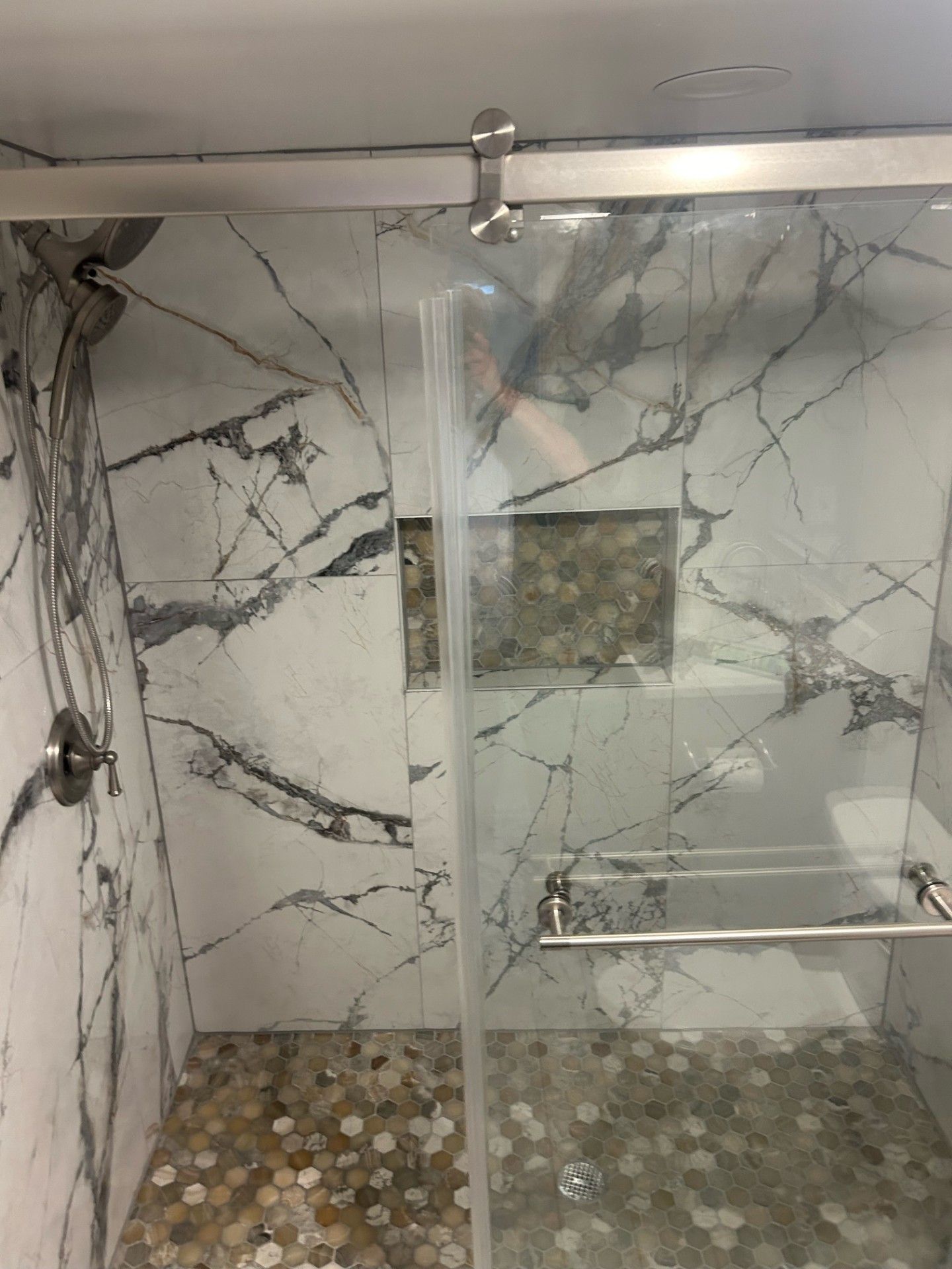 Shower with marble-patterned walls, a glass door, and a pebble tile floor.