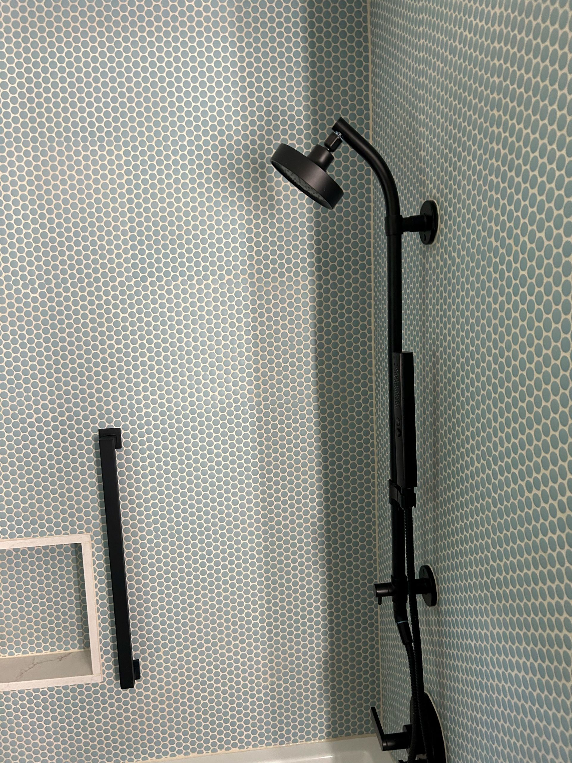 Black shower head and grab bar on a blue-tiled wall.