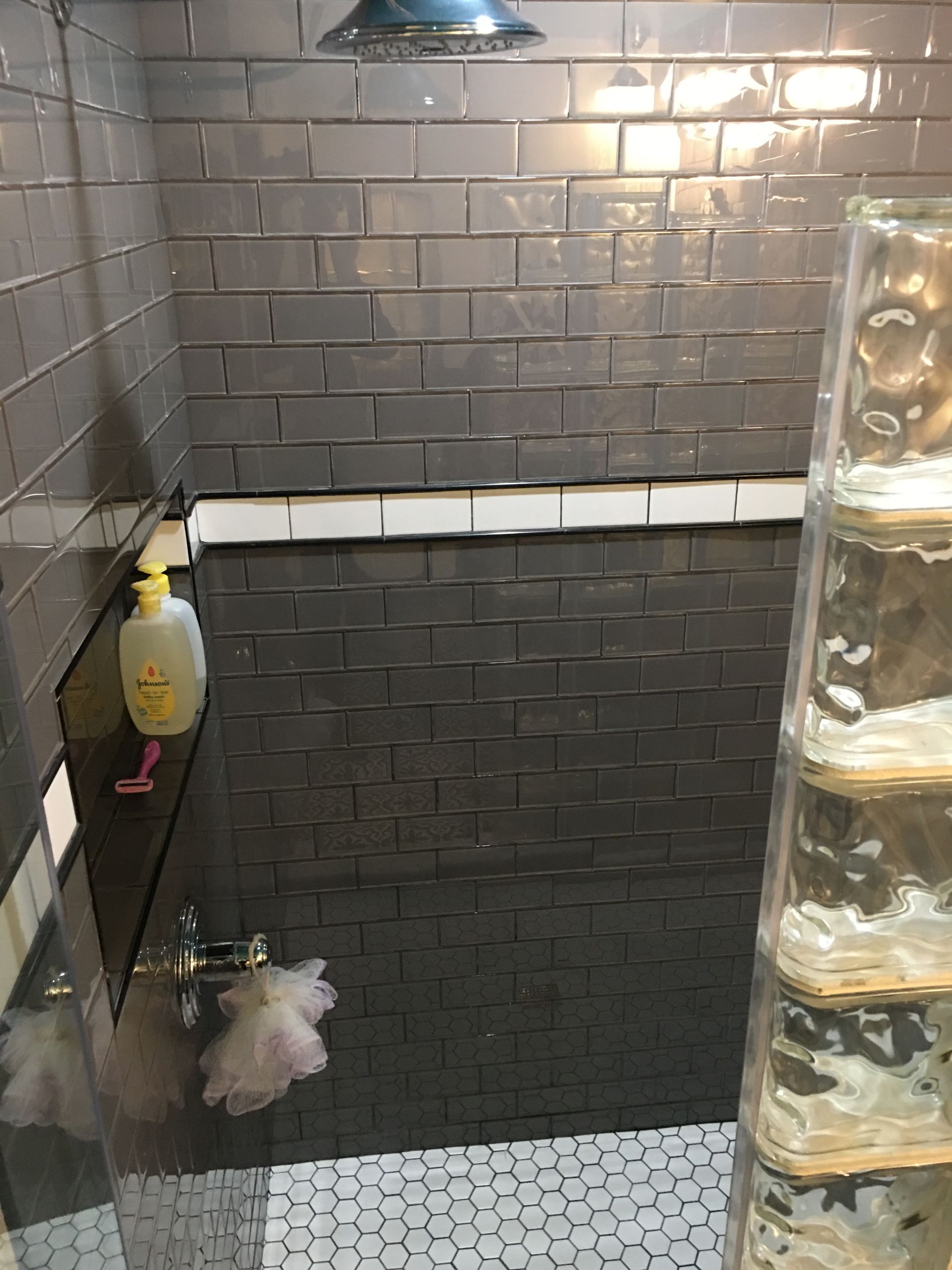 Gray tiled shower with glass block wall; a bottle of lotion and a loofah on a shelf.