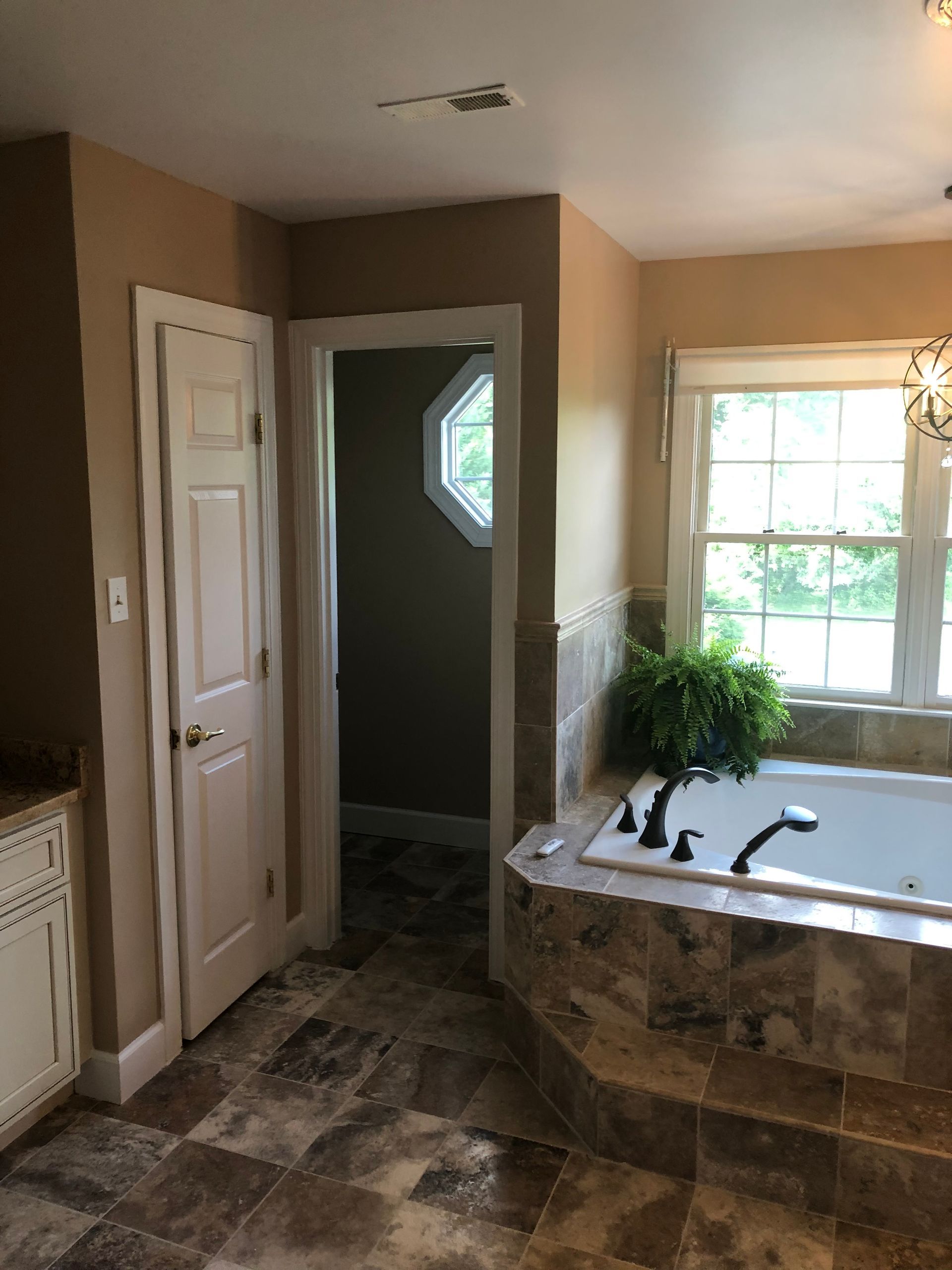 Bathroom with tub, window, door, and vanity. Beige walls, tile floor.