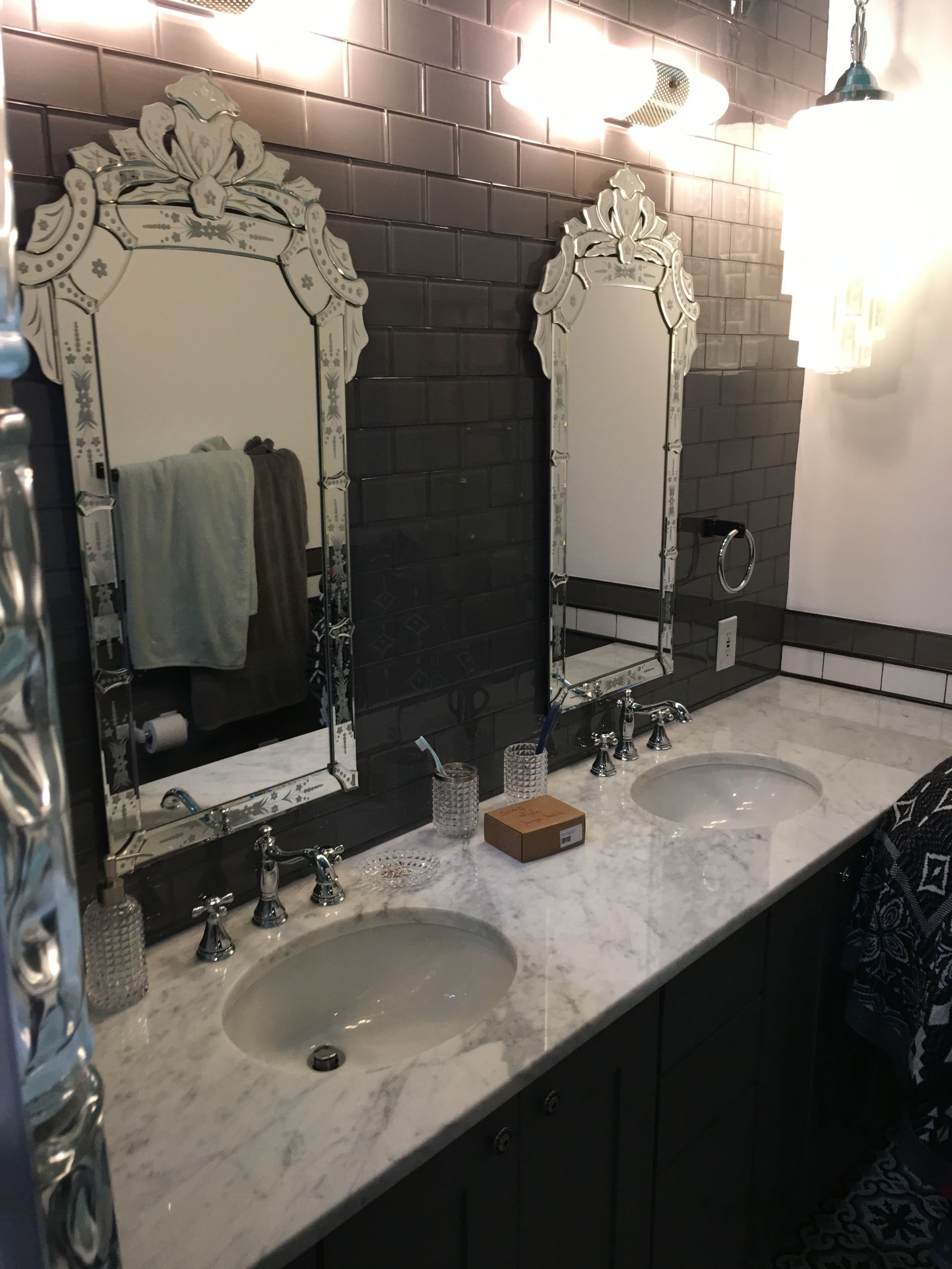 Bathroom with two ornate mirrors, sinks, dark gray tiled wall, and marble countertop.
