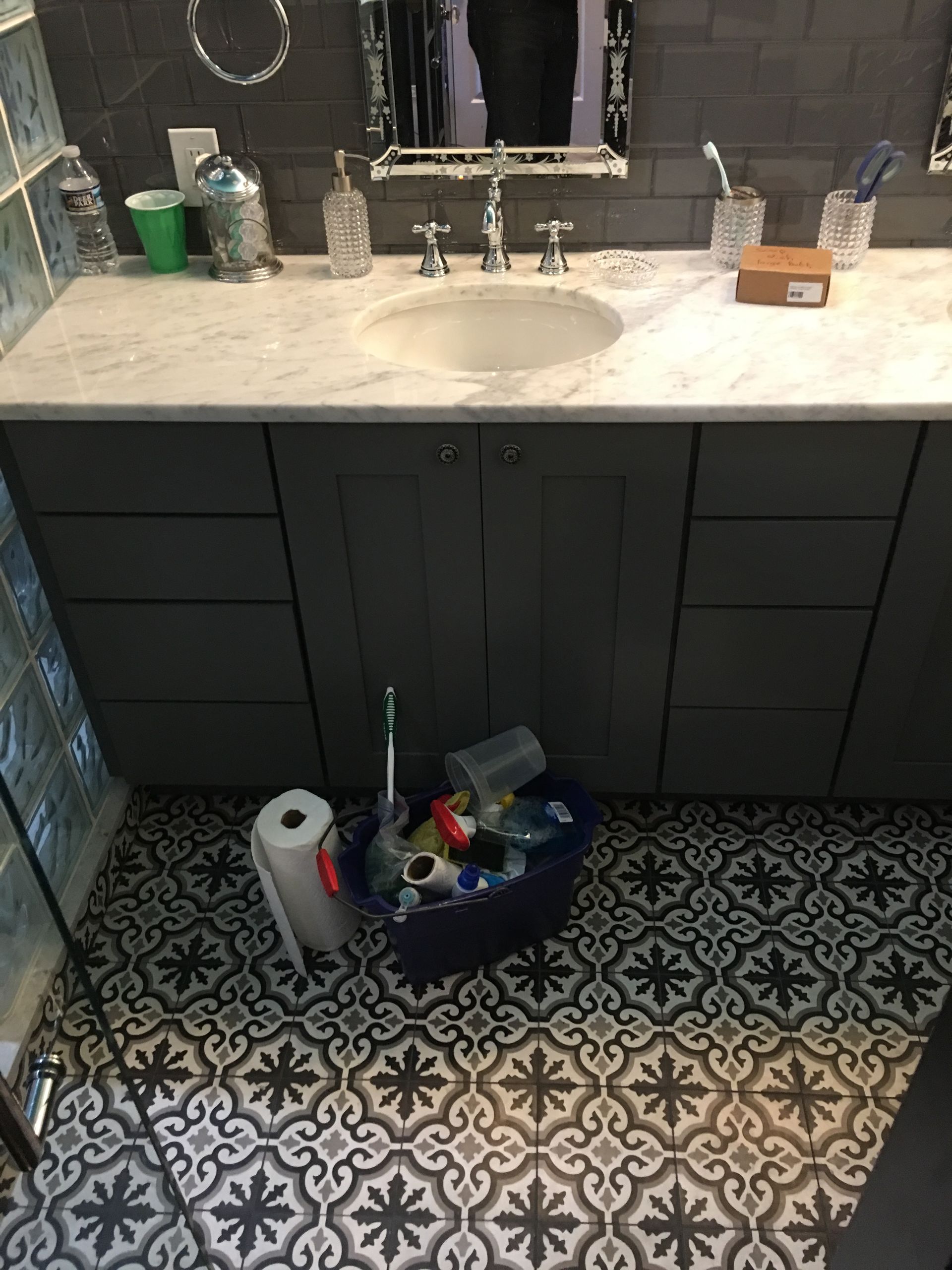 Bathroom with dark gray vanity, marble countertop, patterned floor, and trash bin.