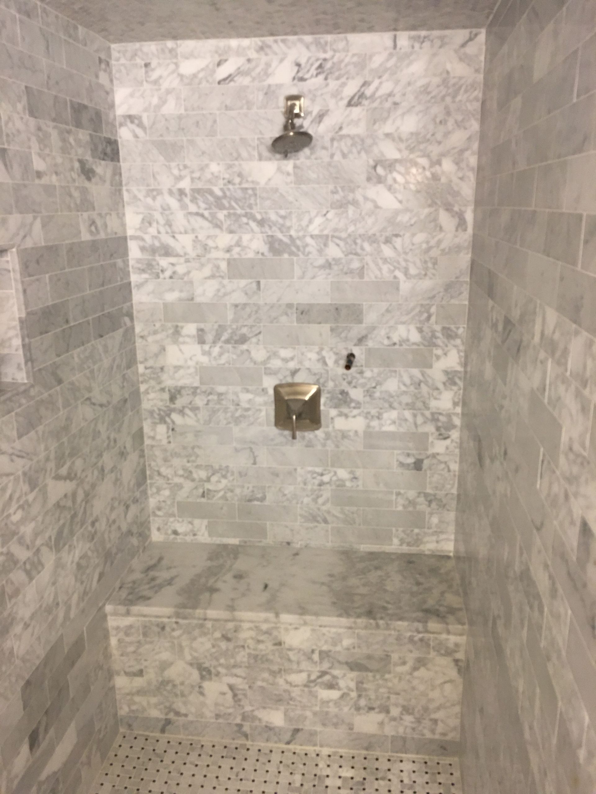 Marble-tiled shower with built-in seat, featuring a showerhead and faucet, in a gray-and-white color scheme.