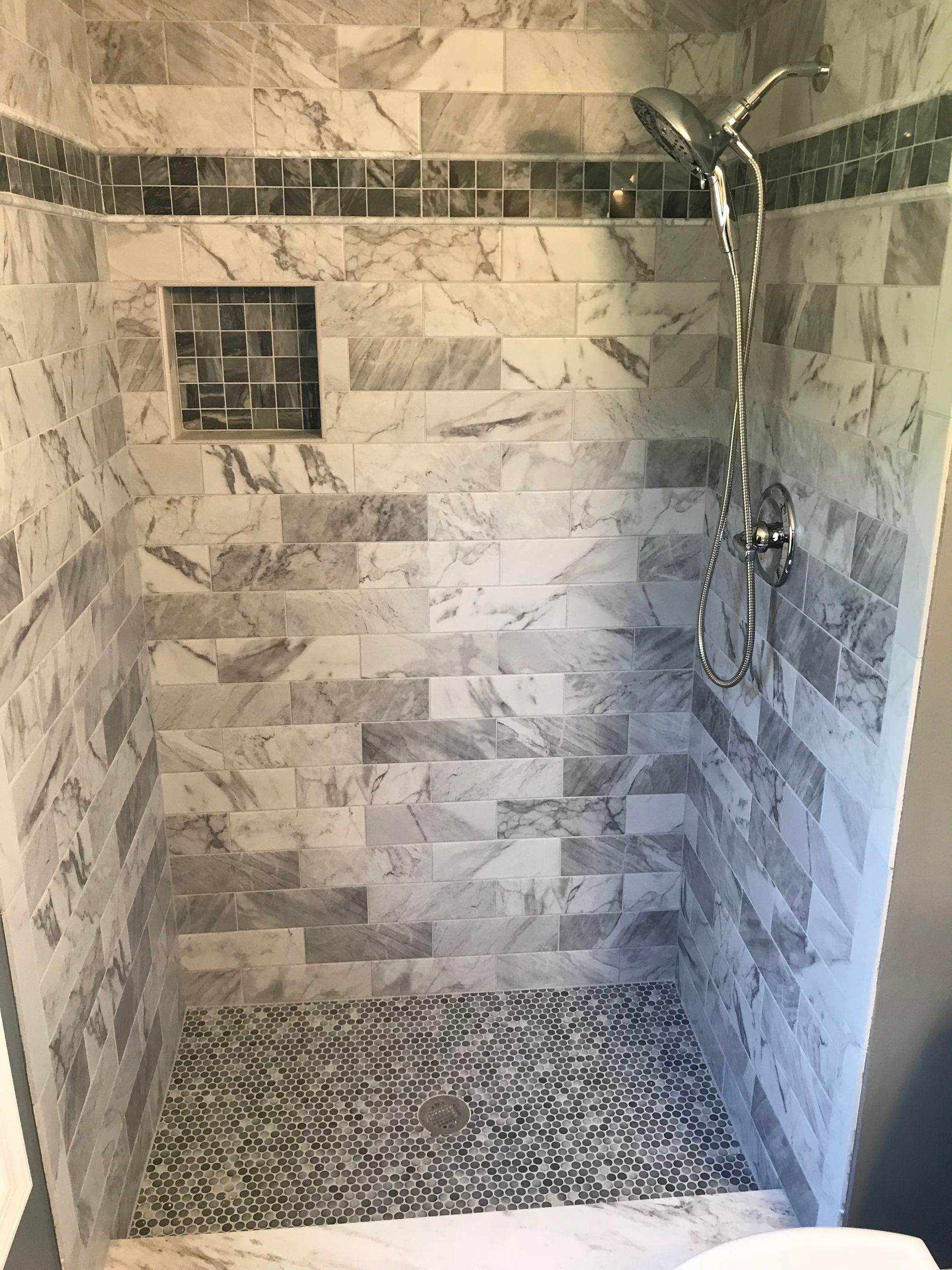 Shower stall with marble tile walls, pebble floor, and a built-in shelf.