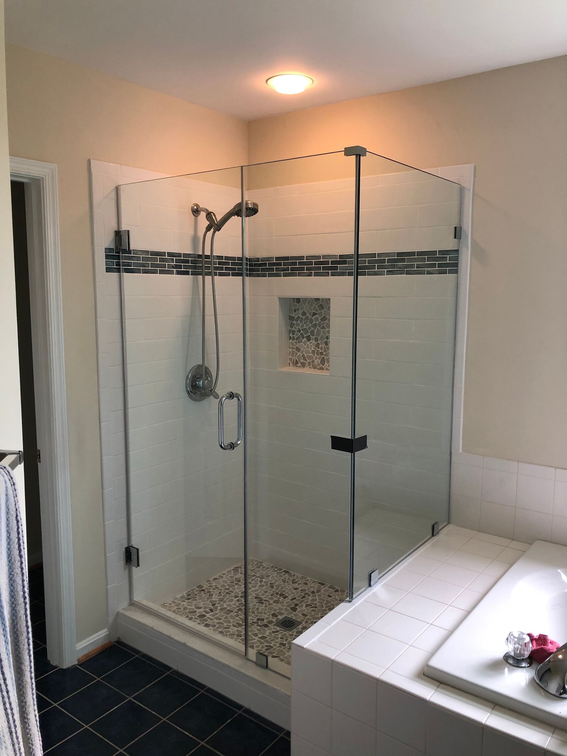 Glass shower with white tile walls, river rock floor, and decorative tile border.