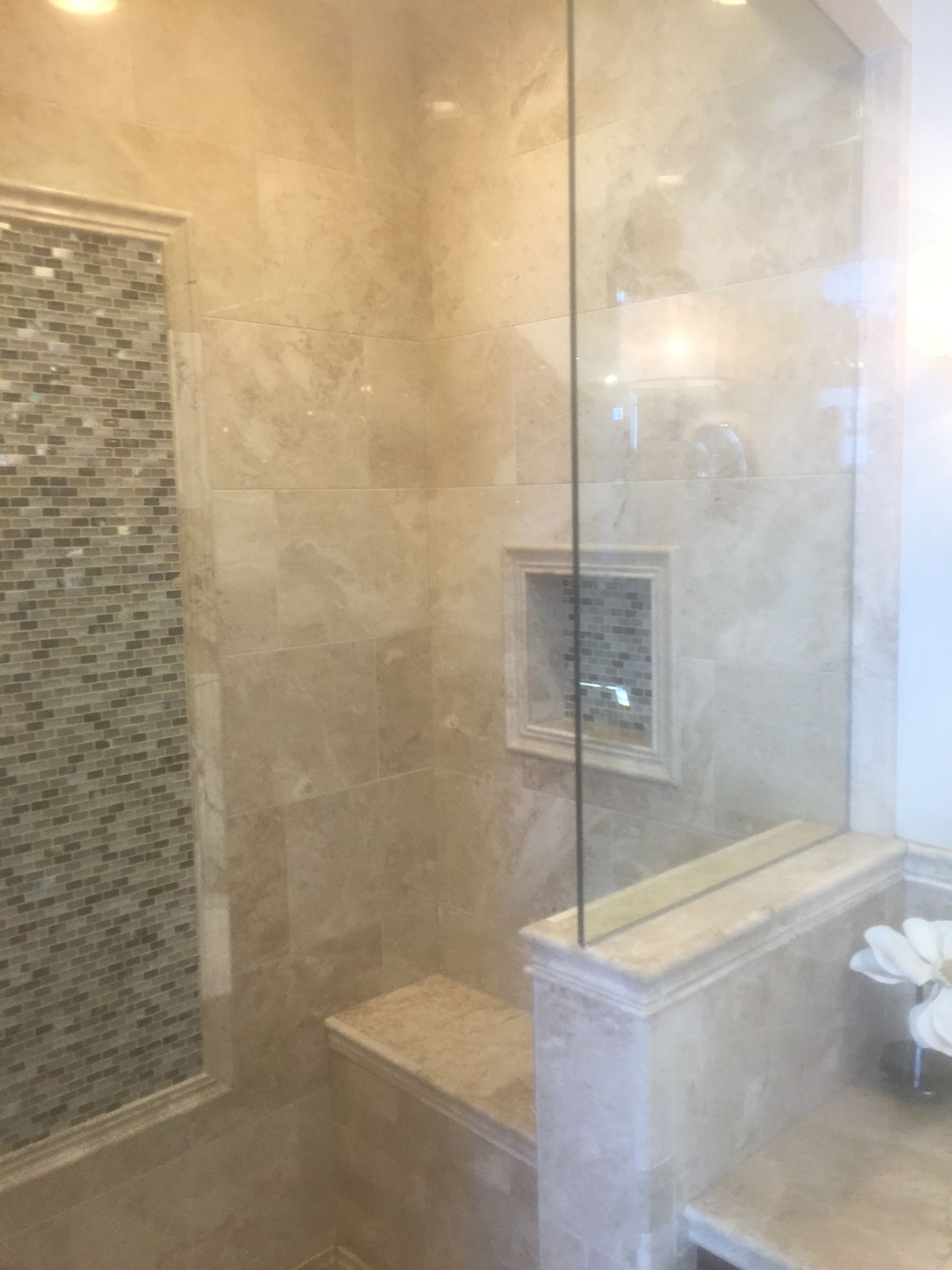 Shower with glass door, marble walls, built-in bench, and tiled niche.