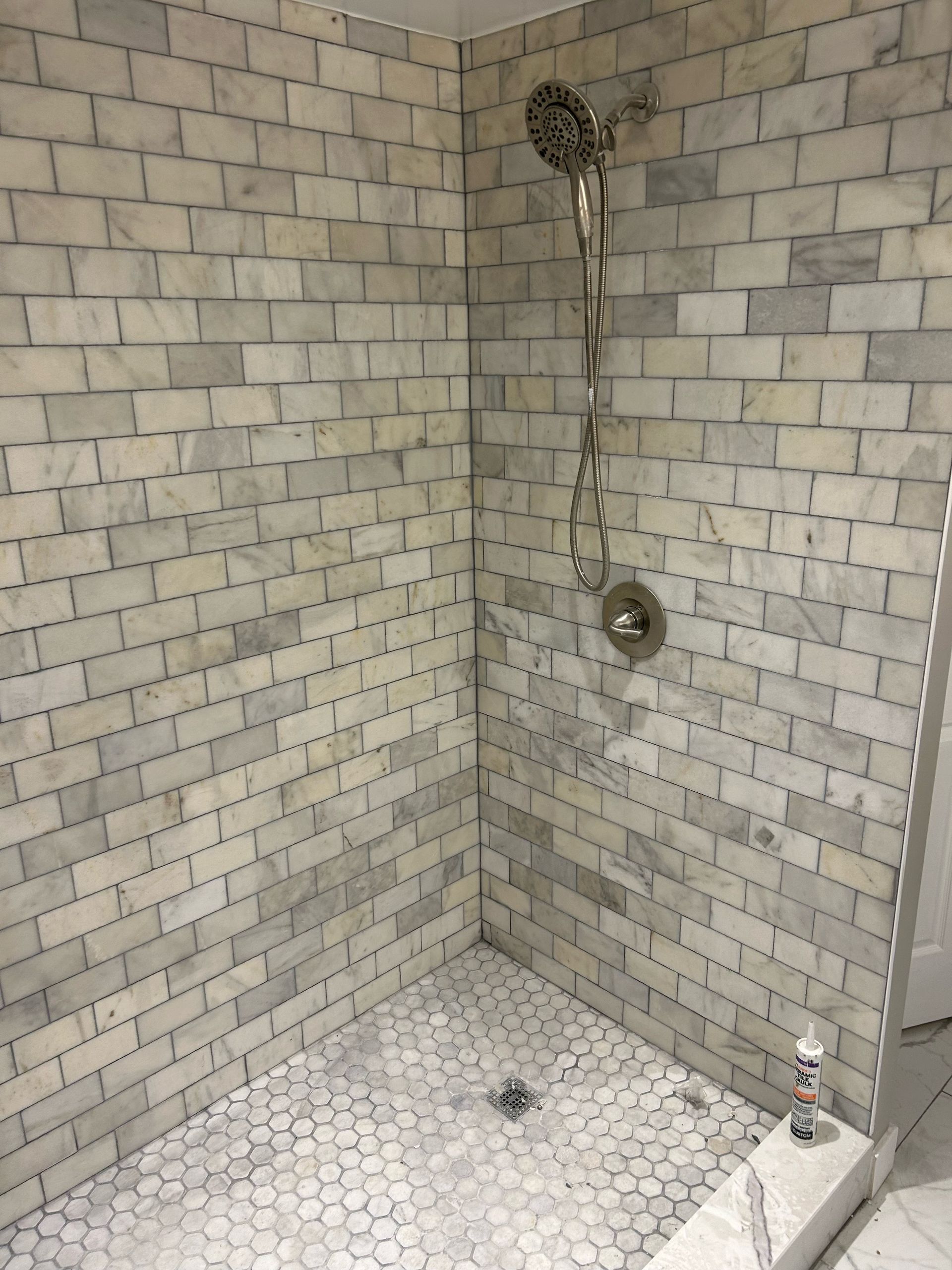 Marble-tiled shower with hexagon floor. Includes showerhead and faucet.