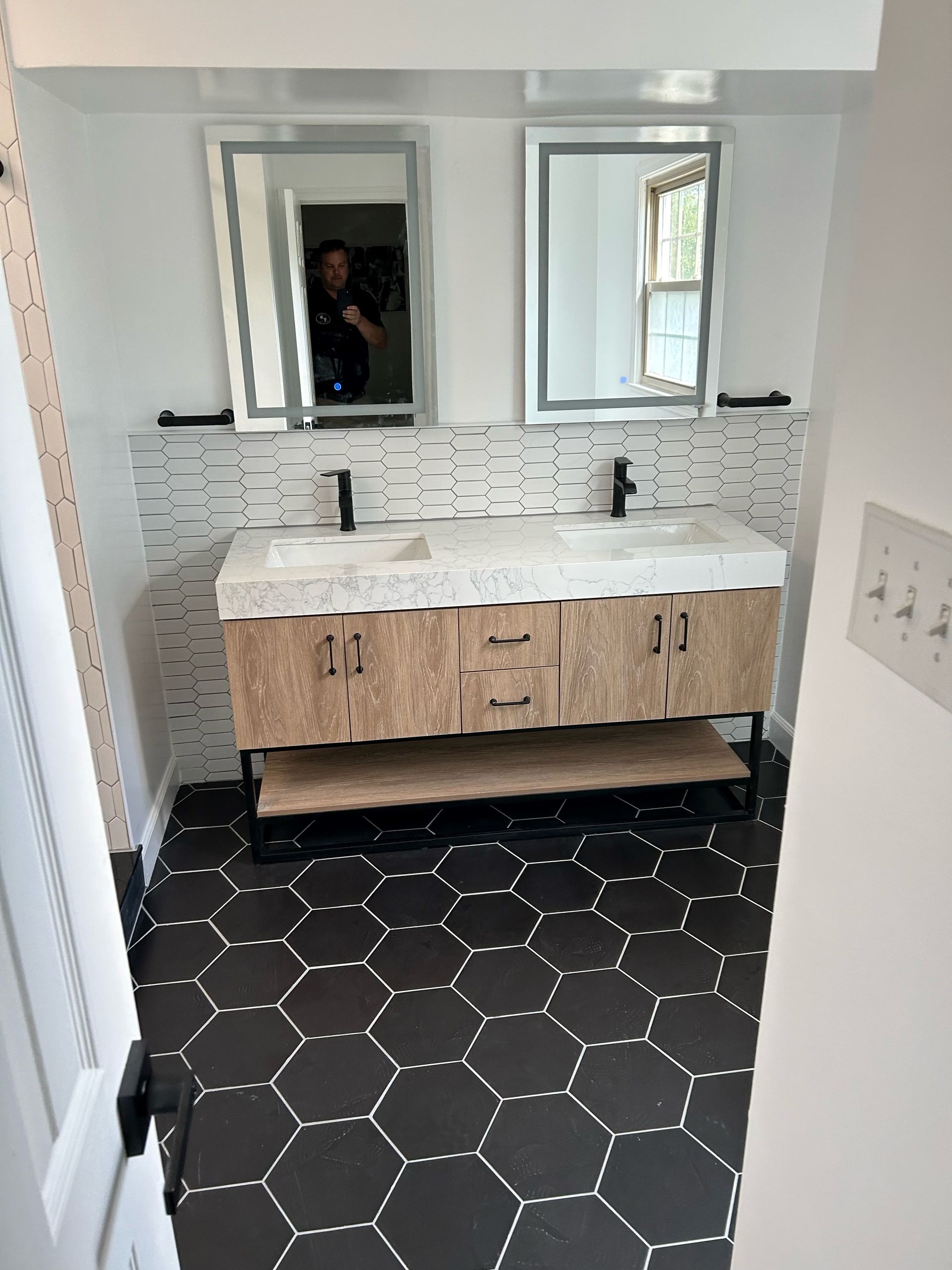 Bathroom with wooden vanity, black fixtures, hexagon tile floor, and two mirrors.