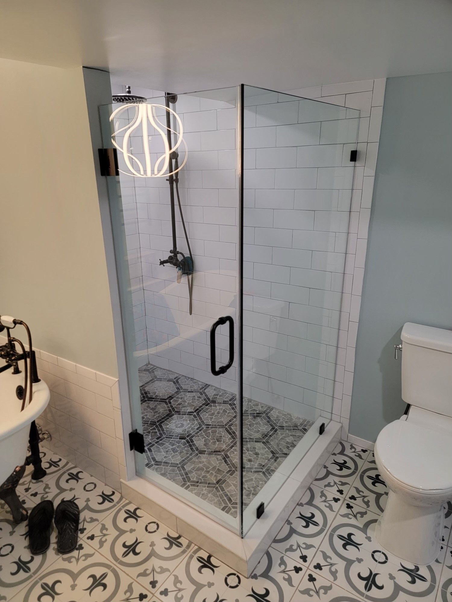 A modern bathroom with a glass shower, black fixtures, and patterned tile flooring.