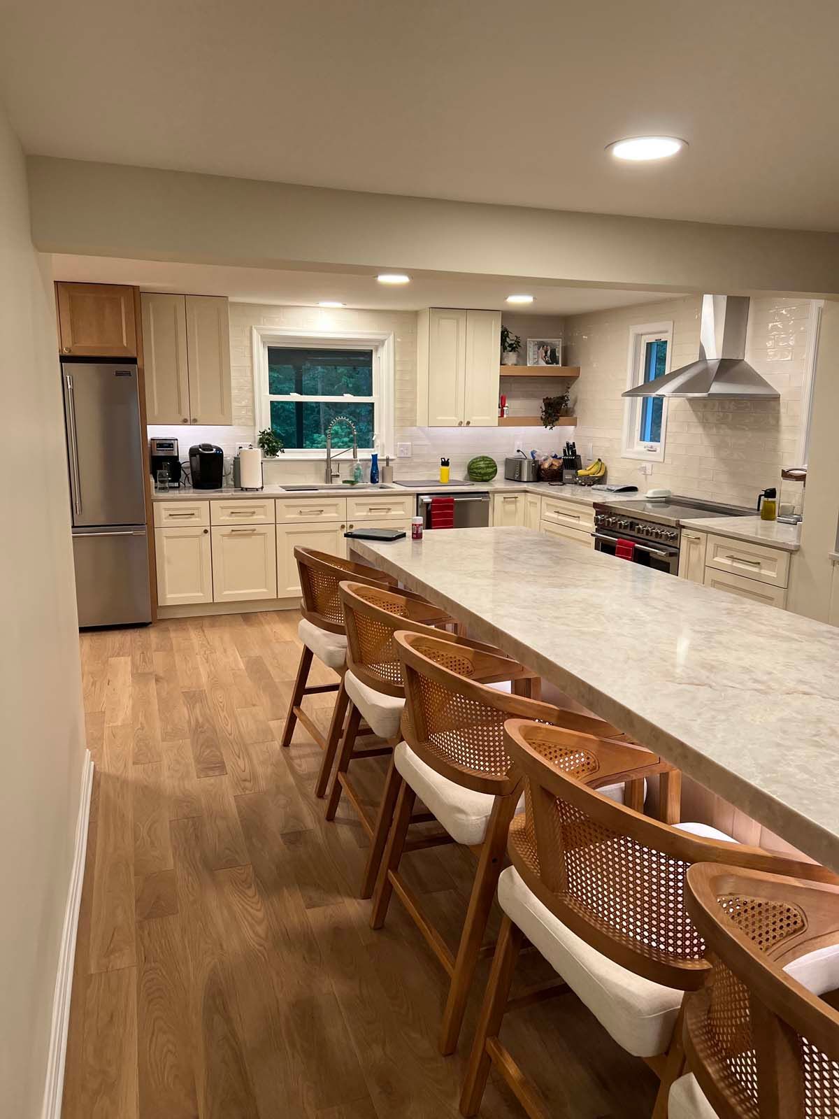 Spacious modern kitchen with a long island, wood floors, and rattan bar stools.