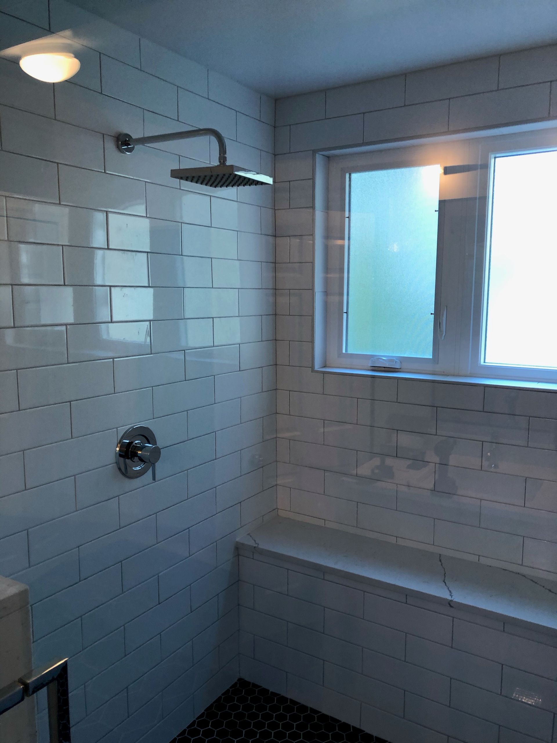 Shower with white subway tiles, a window, and a built-in bench. Chrome showerhead and faucet.