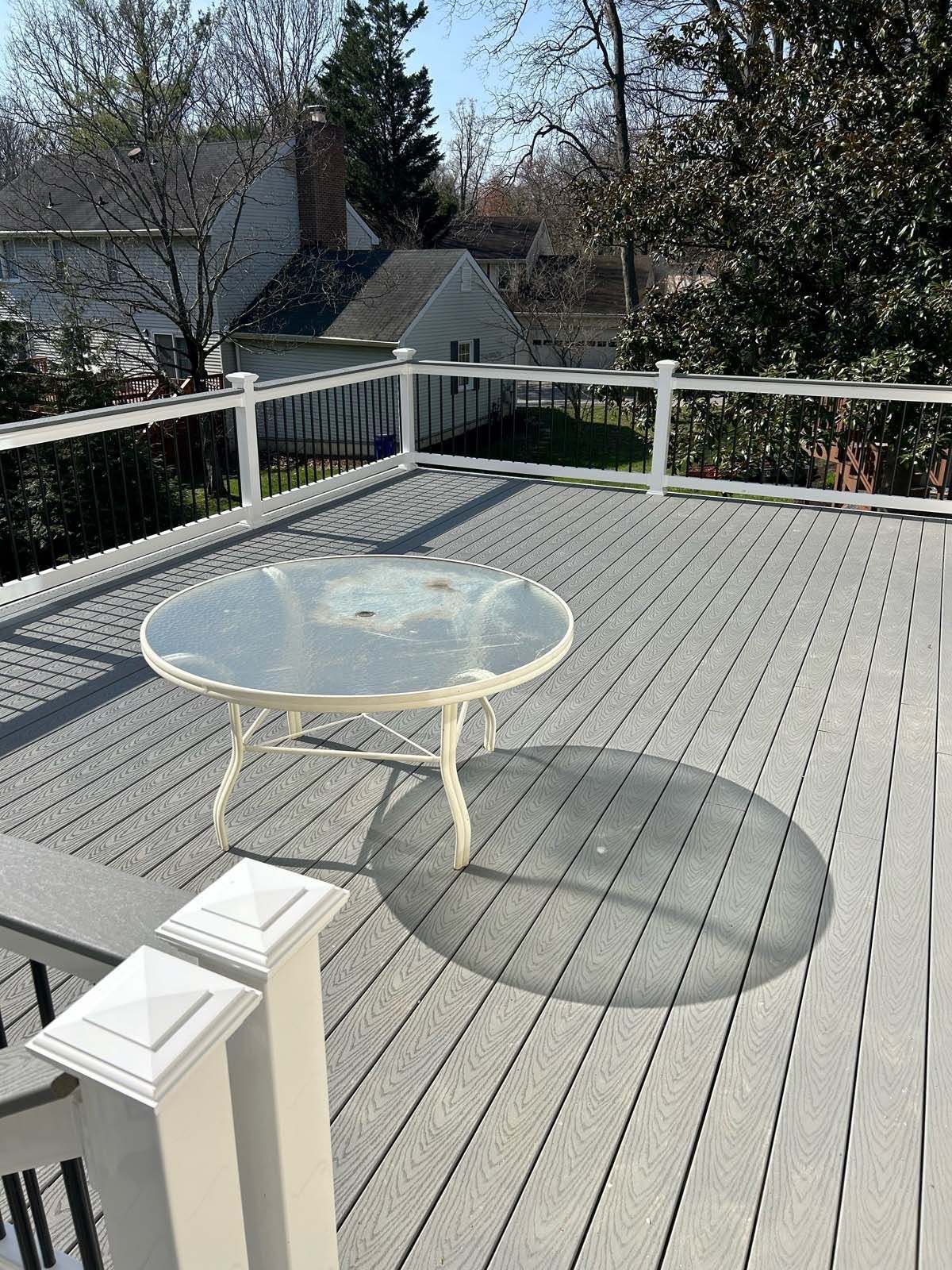 Gray composite deck with a round glass table; a white railing surrounds the deck.