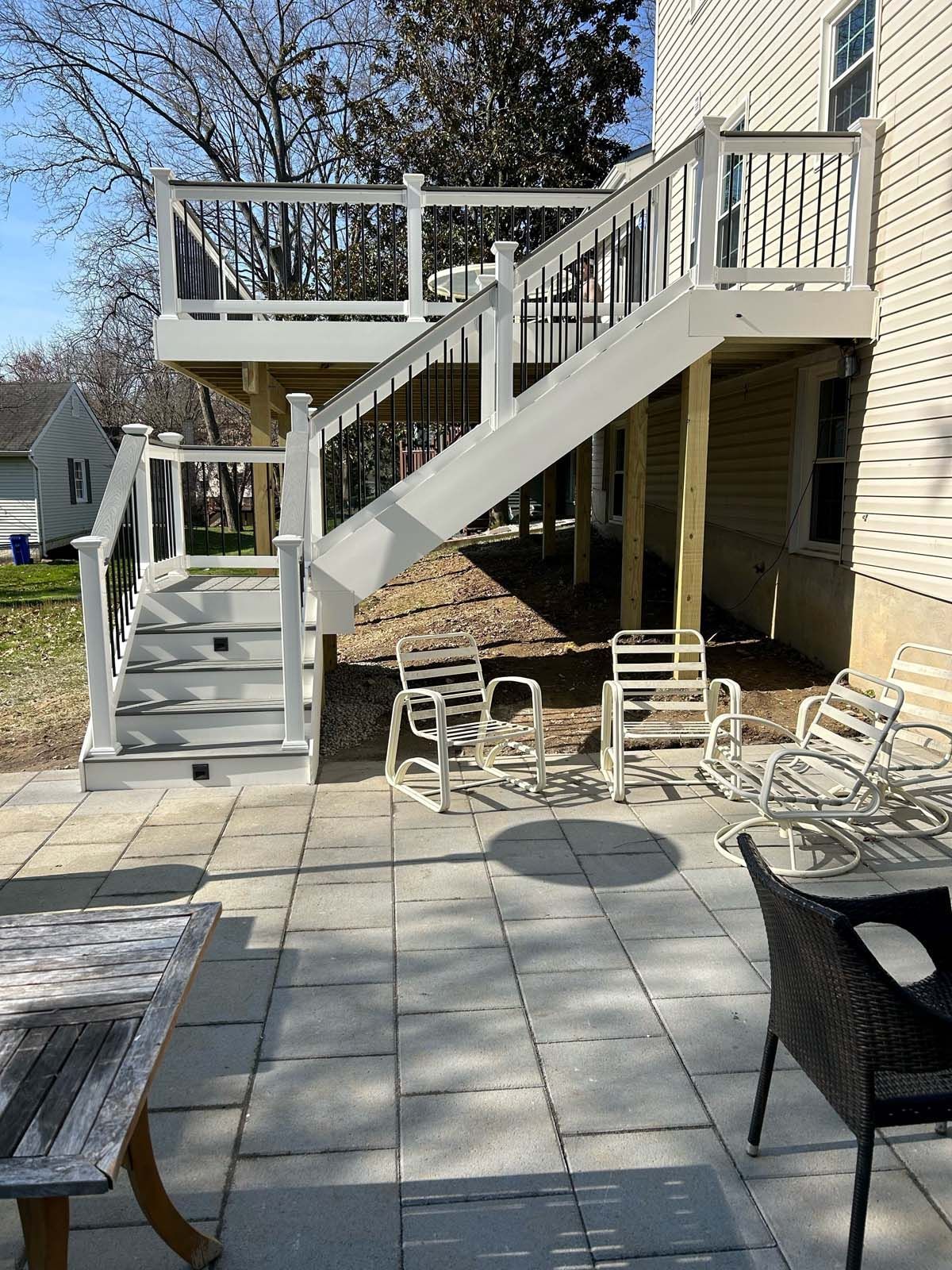 Two-level deck with stairs, white railings, and a patio with furniture next to a house.