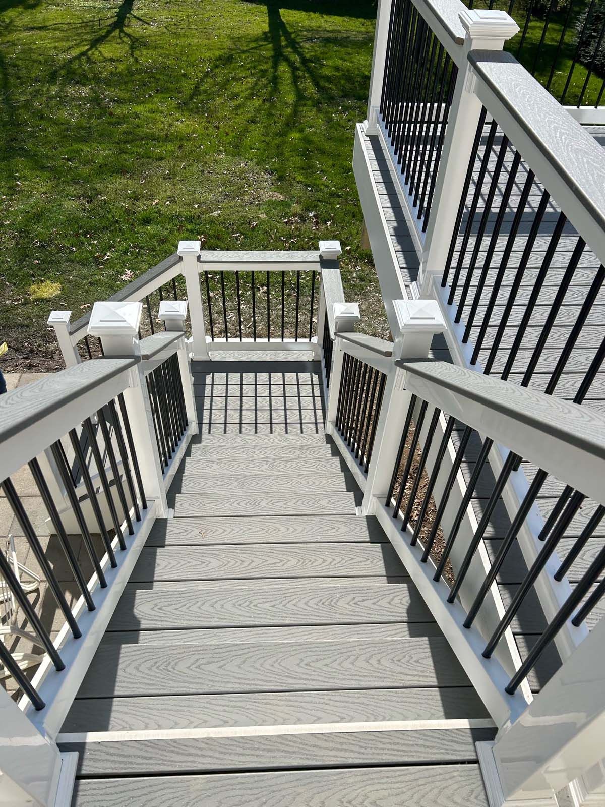 Gray wooden stairs with white railing and black balusters leading down to a grassy yard.