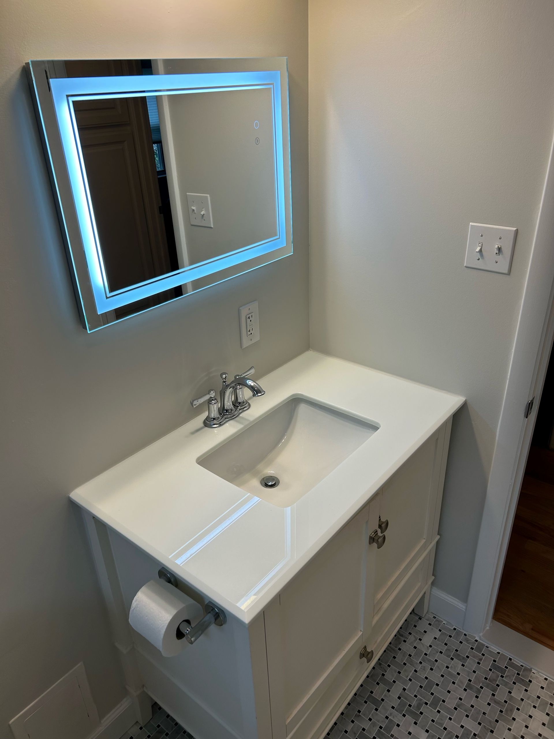 White bathroom vanity with a lit-up mirror, sink, and toilet paper holder.