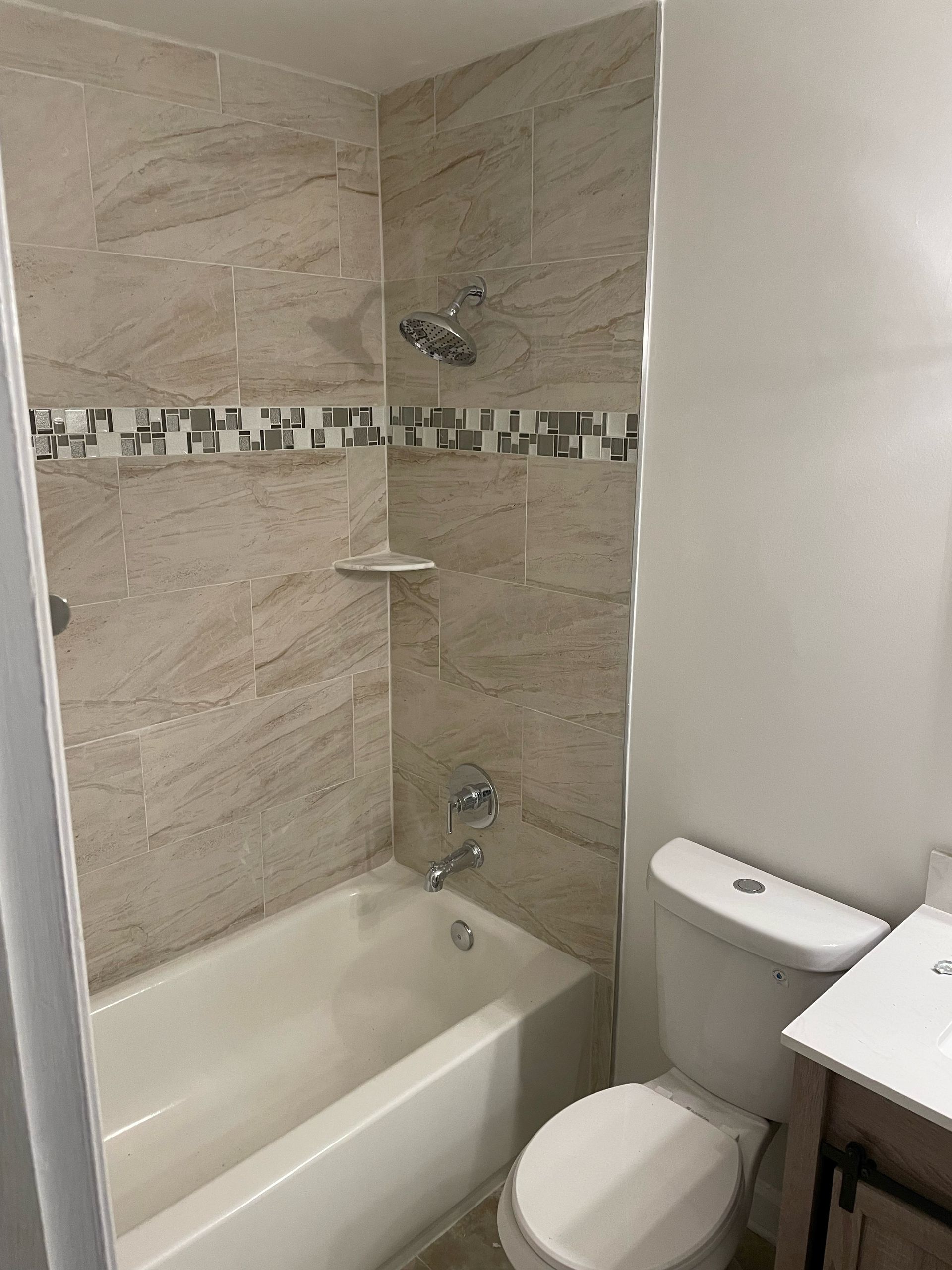 Bathroom with beige tiled shower, tub, toilet, and vanity; decorative tile border.
