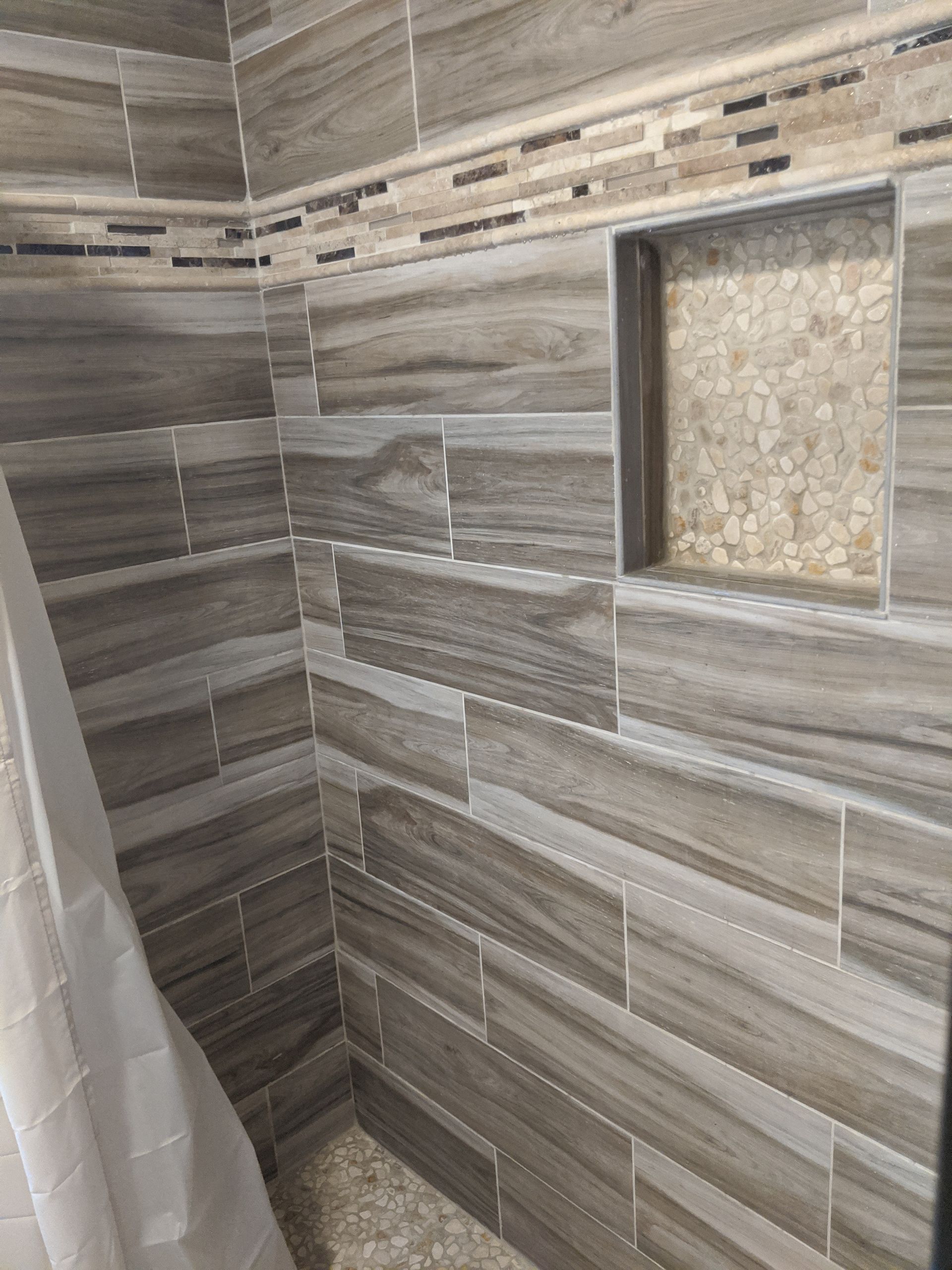 Shower tiled with wood-look gray tile, featuring a decorative mosaic accent and built-in shelf.