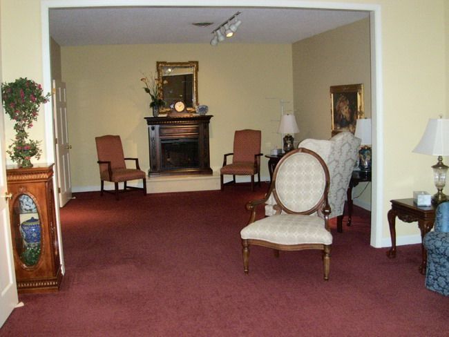 A room with a fireplace, chairs, and a burgundy carpet.