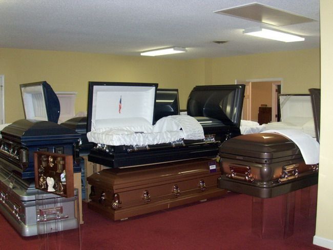 Casket display room with multiple open and closed caskets, various colors.