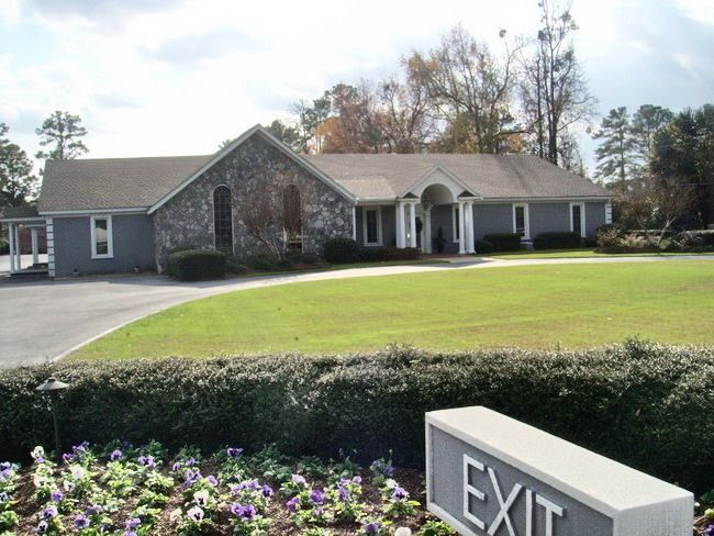 Exterior view of a stone and gray building with a lawn, sign reading 