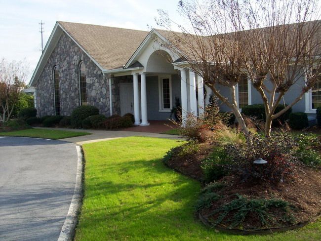 Stone and gray building with columns, lawn, and bare tree in front.
