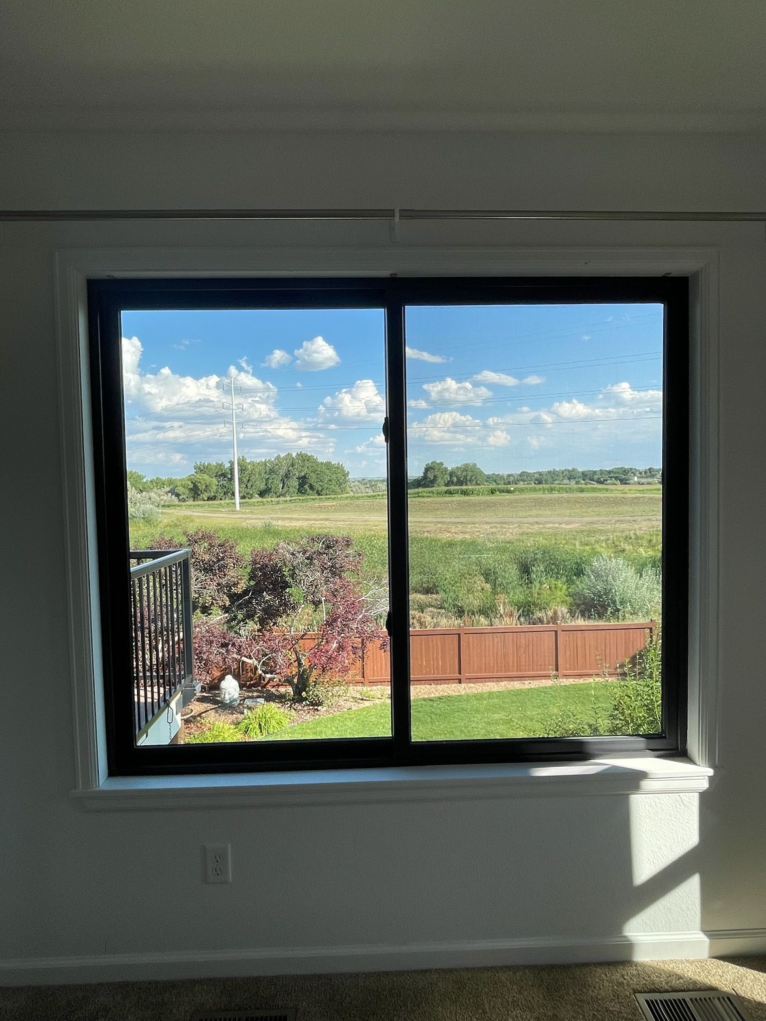 Sliding window with black frame, showing a sunny sky and a green field.