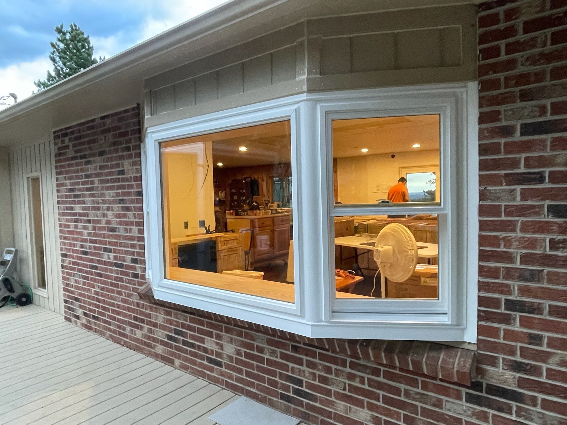 Bay window with white trim on a brick house. Interior visible with a person.