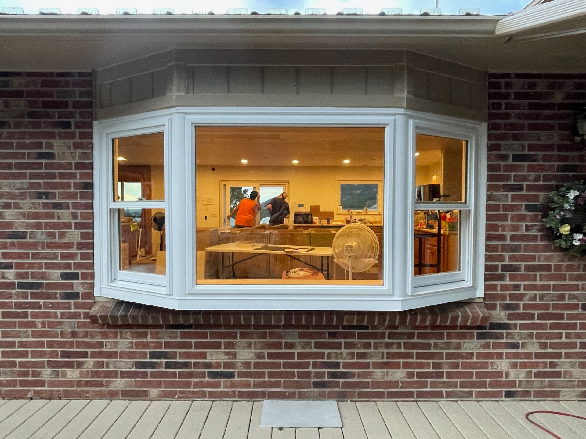 Bay window on a brick building, with interior visible. White trim, neutral siding above. Deck in foreground.