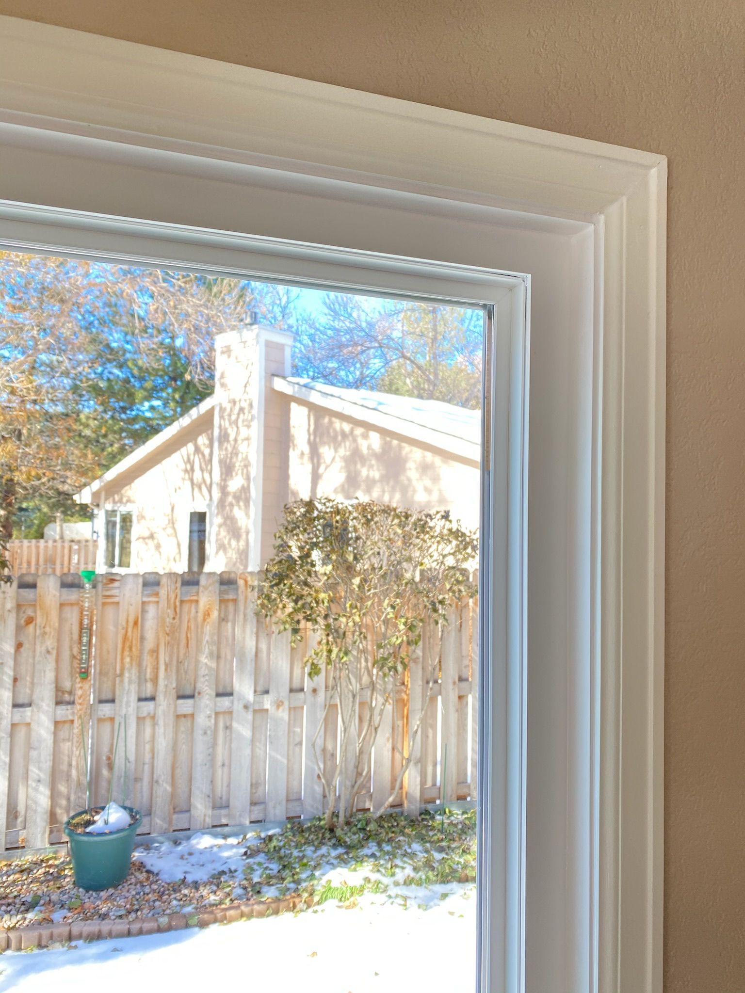 White window frame with view of a snow-covered yard, wooden fence, and house.