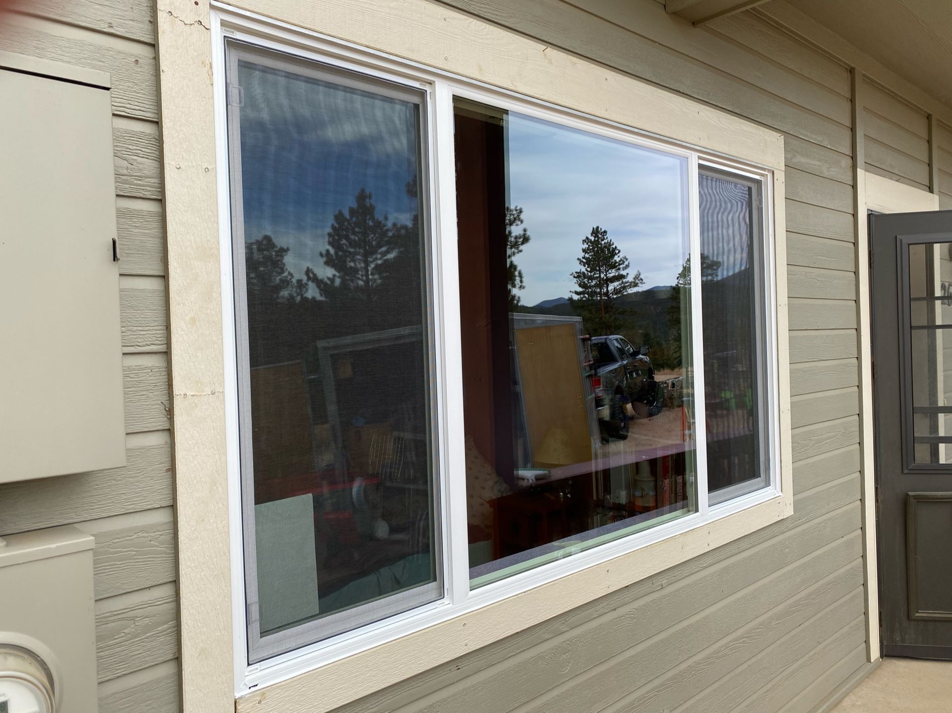 Exterior view of a sliding window with white frame, screen, and visible trees.