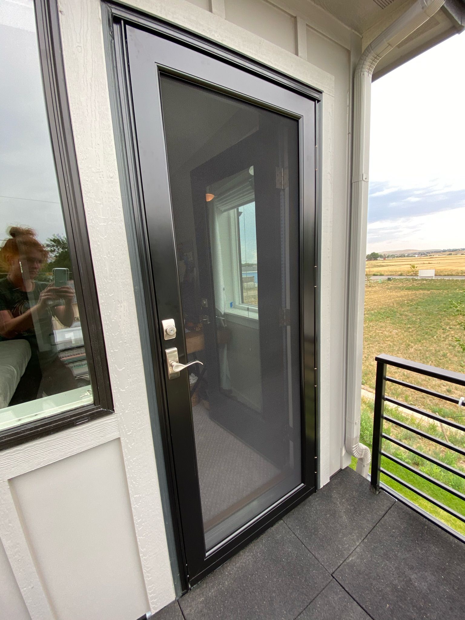 Black screen door on a white house, leading to an outdoor area with a railing and open view.