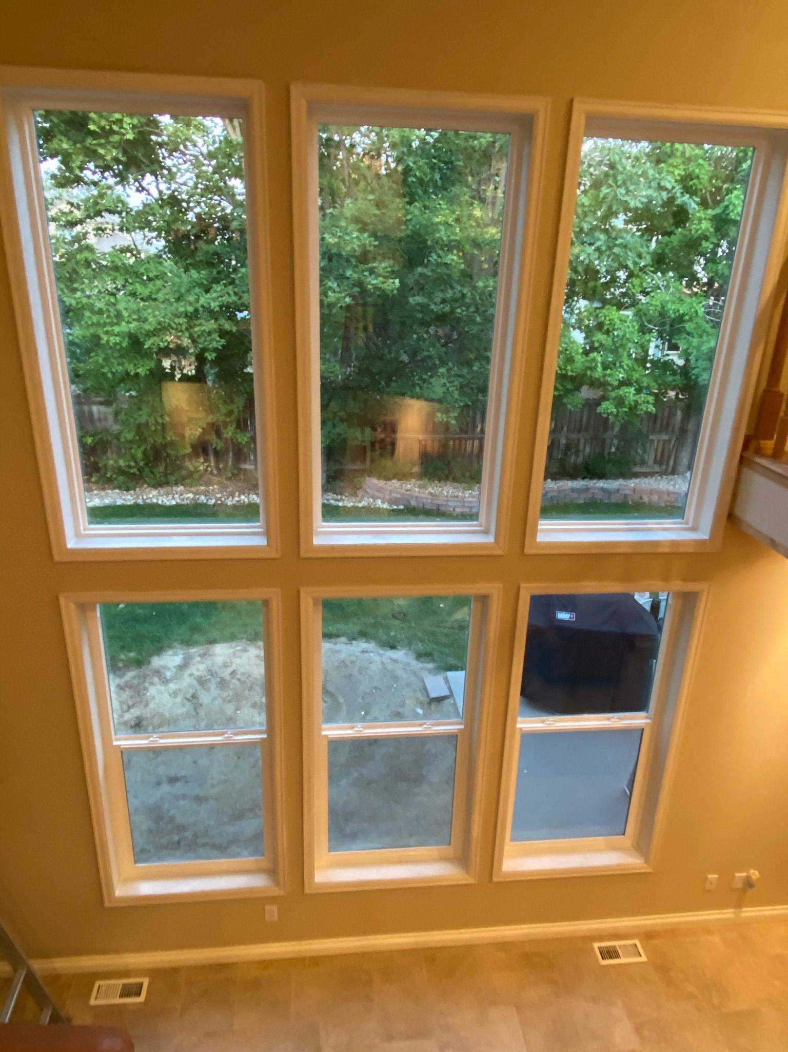 Six tall windows in a light-colored room offer a view of green trees.