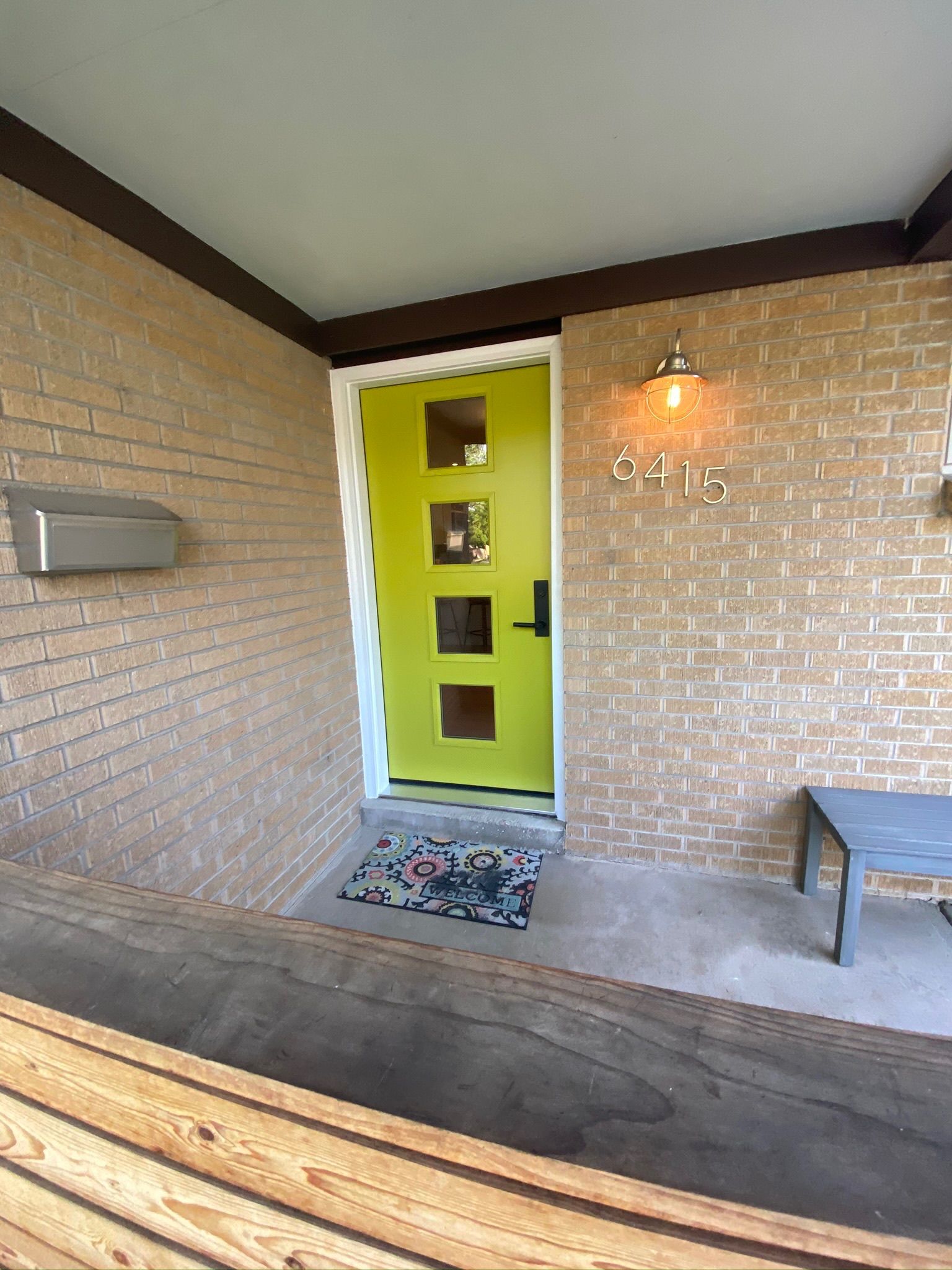 Bright yellow front door with four square windows, brick exterior, and a silver mailbox.