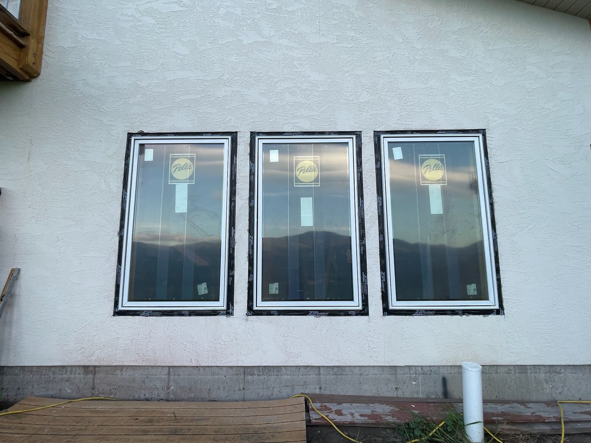 Three rectangular windows installed in a stucco wall, sealed with black tape.