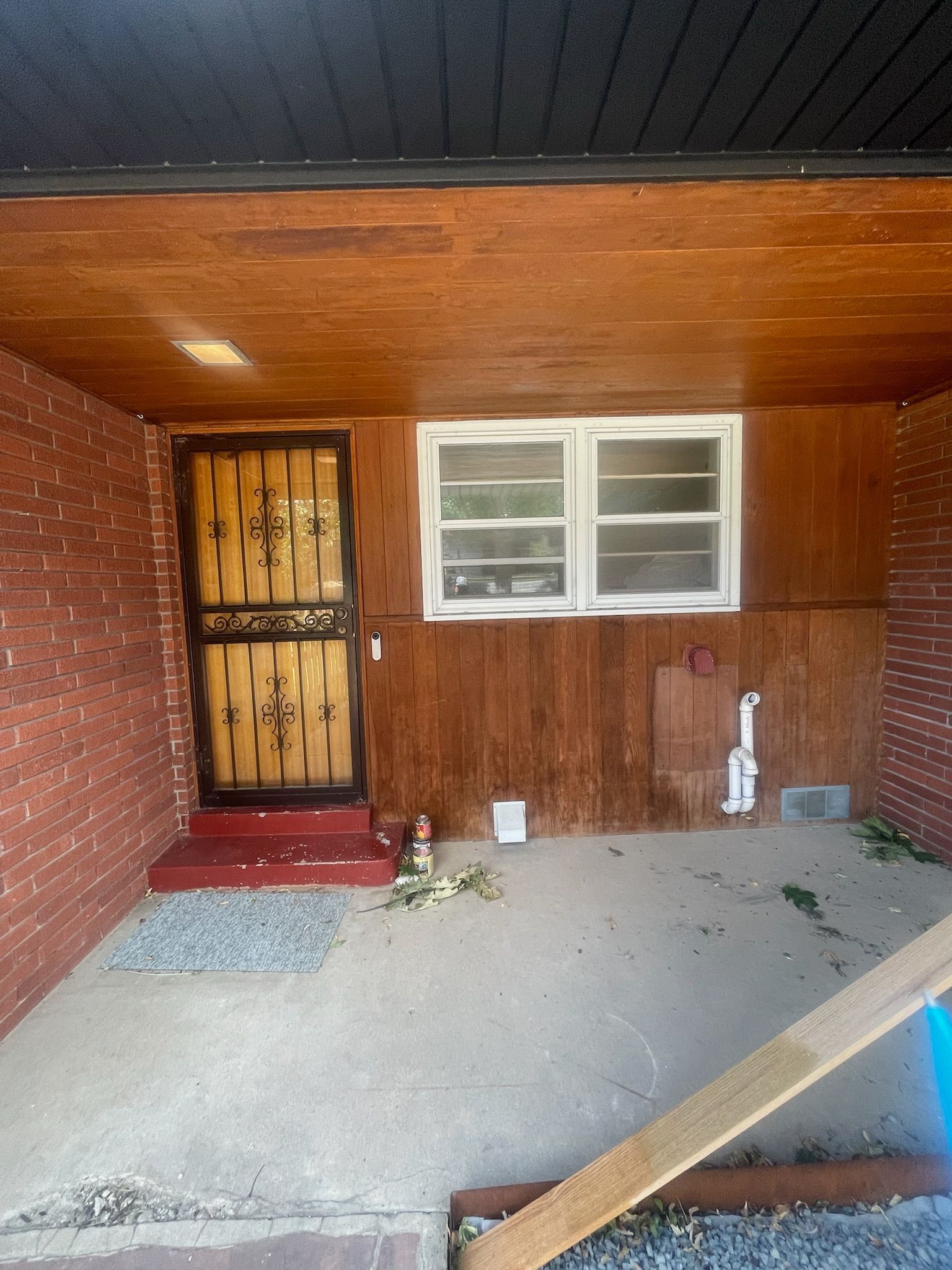Covered porch with brick walls, a wooden ceiling, and a security door with a window and a small window to the right.