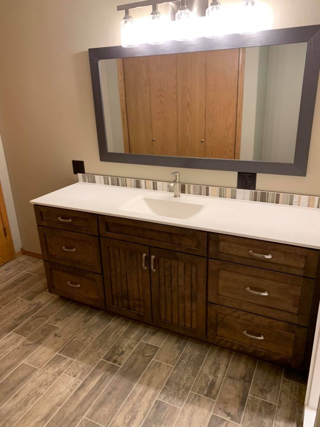 A bathroom with a sink , mirror and wooden cabinets.