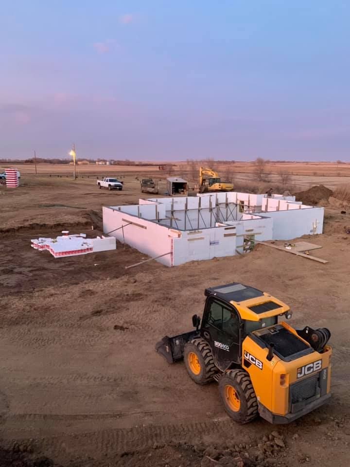 A bulldozer is driving down a dirt road in front of a building under construction.