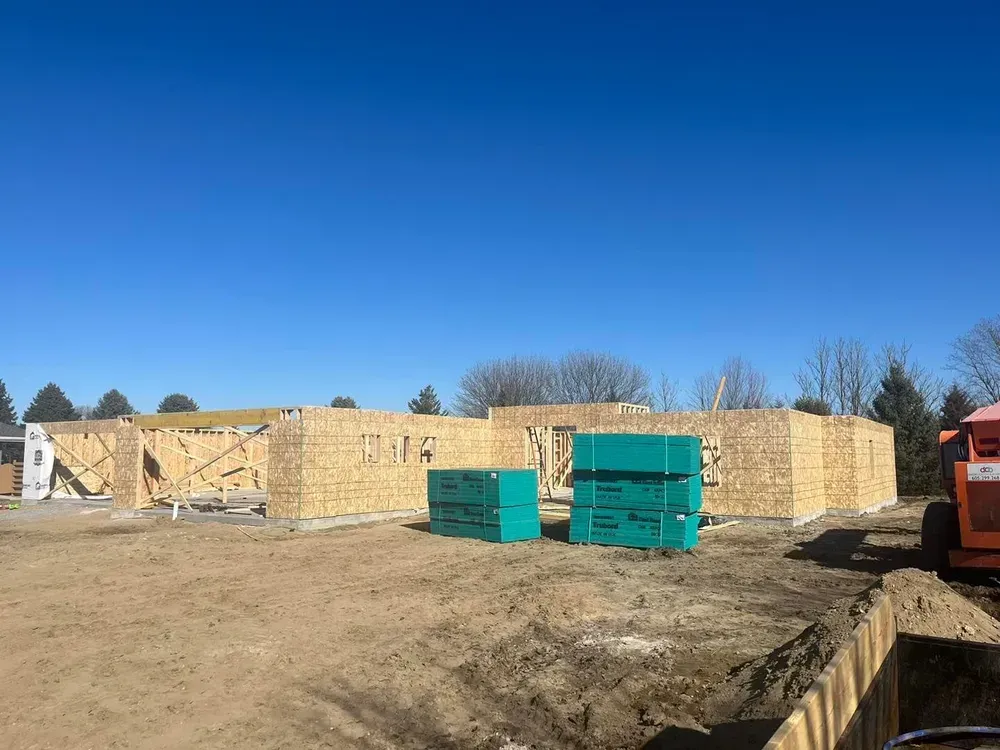 A house is being built in a dirt field with a blue sky in the background.