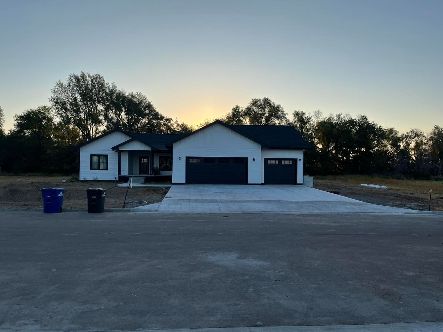 A white house with a black roof is sitting on top of a dirt field.