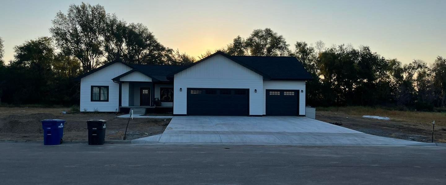 A white house with a black roof is sitting on top of a dirt field.