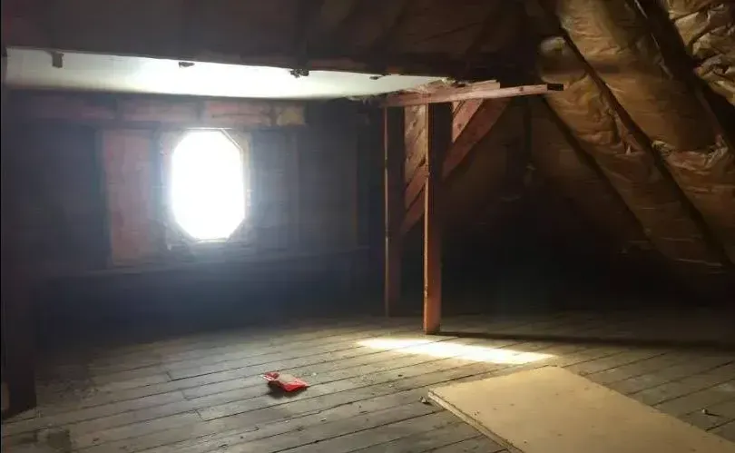 A dark attic with a window and a light coming through it.